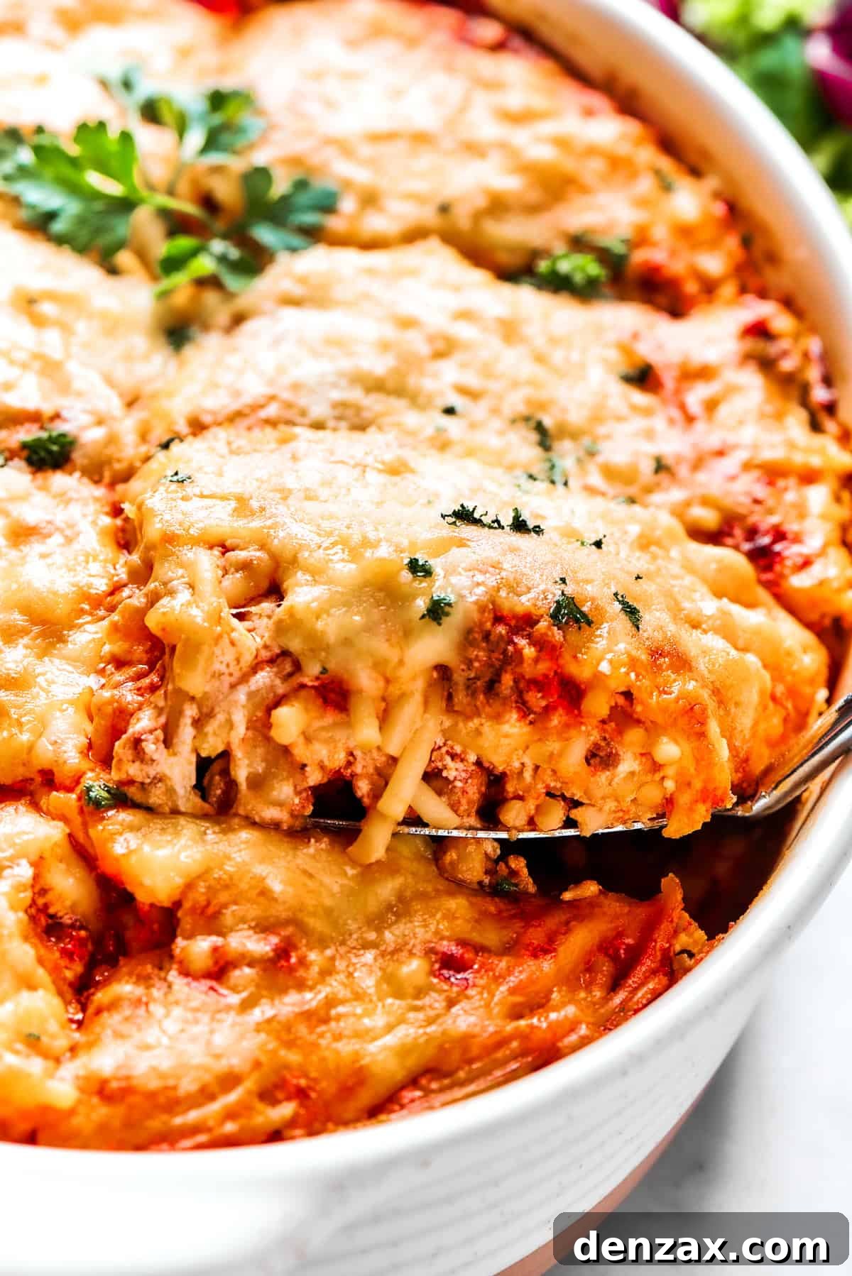 A large serving spoon scooping out a portion of baked million dollar spaghetti from a casserole dish, revealing its cheesy, layered interior.