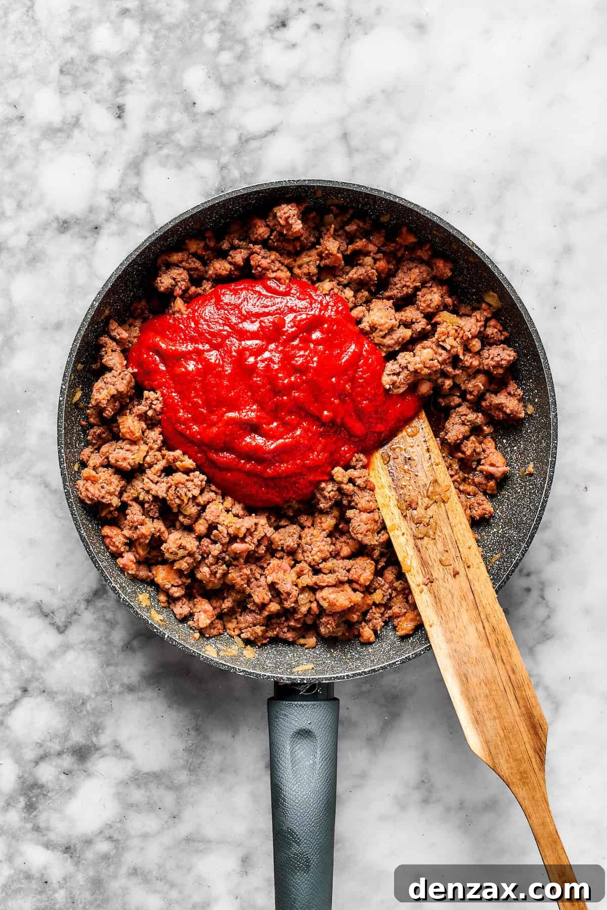 Adding a jar of marinara sauce to the cooked meat mixture in a skillet.