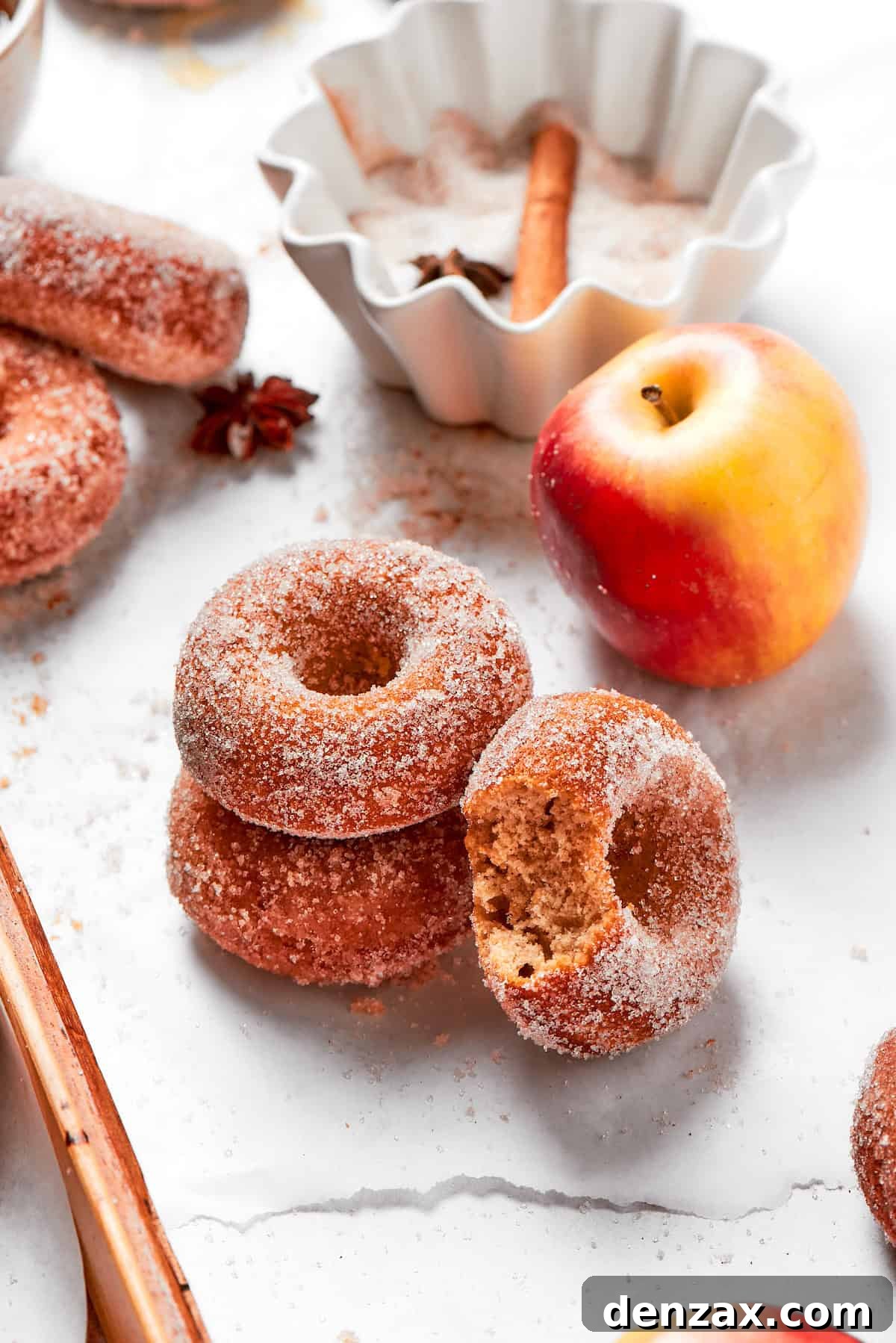 A charming stack of homemade apple cider donuts next to a fresh red apple, evoking cozy fall feelings.