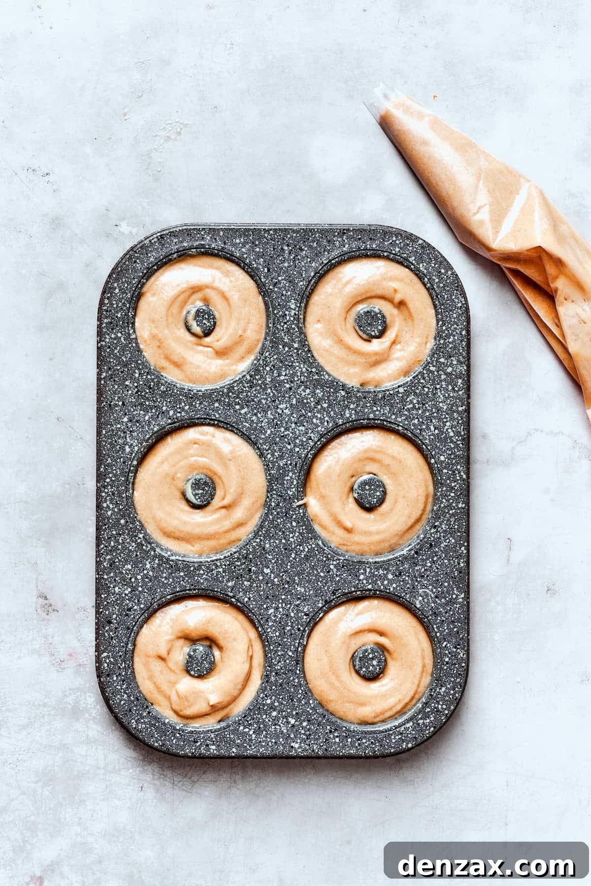 A donut baking pan with batter neatly piped into each well, showing the distinct donut shape before baking.