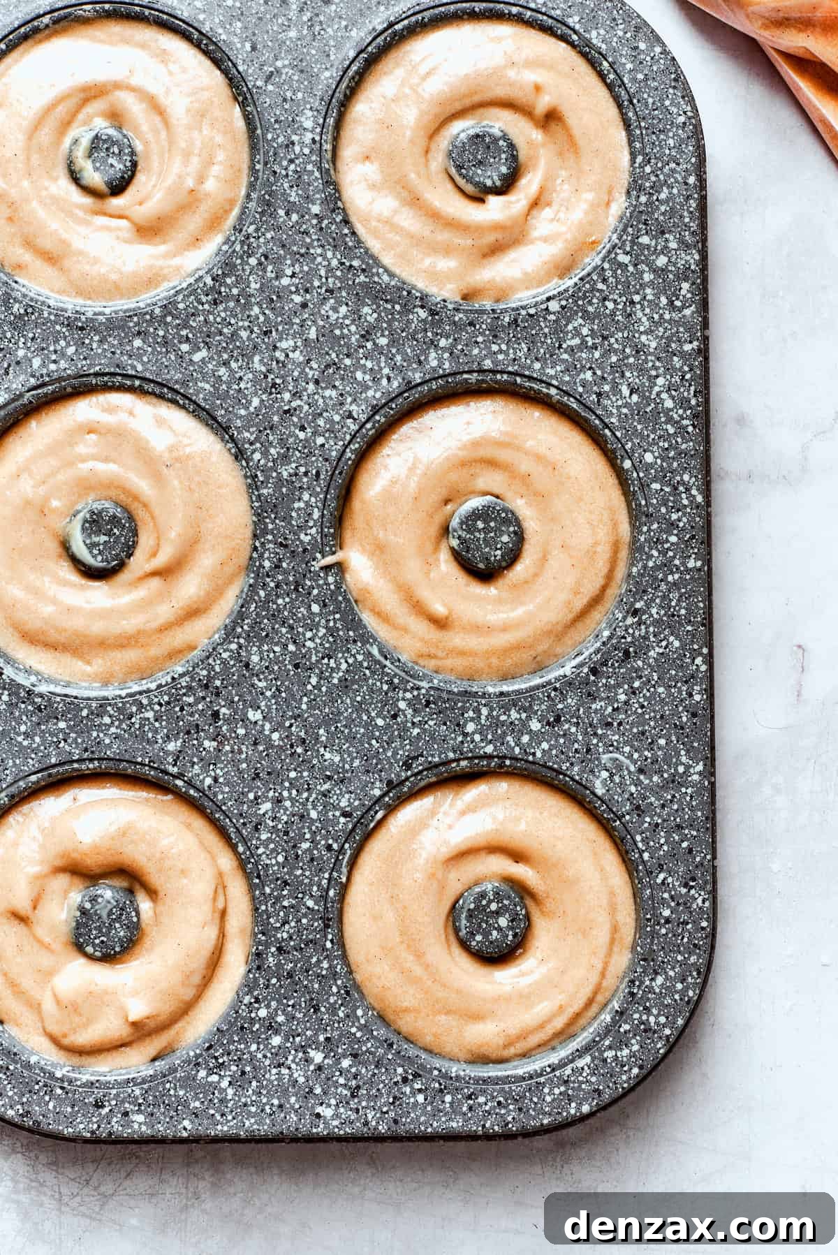 A close-up of apple cider donut batter perfectly portioned in a donut pan, ready to go into the oven for baking.