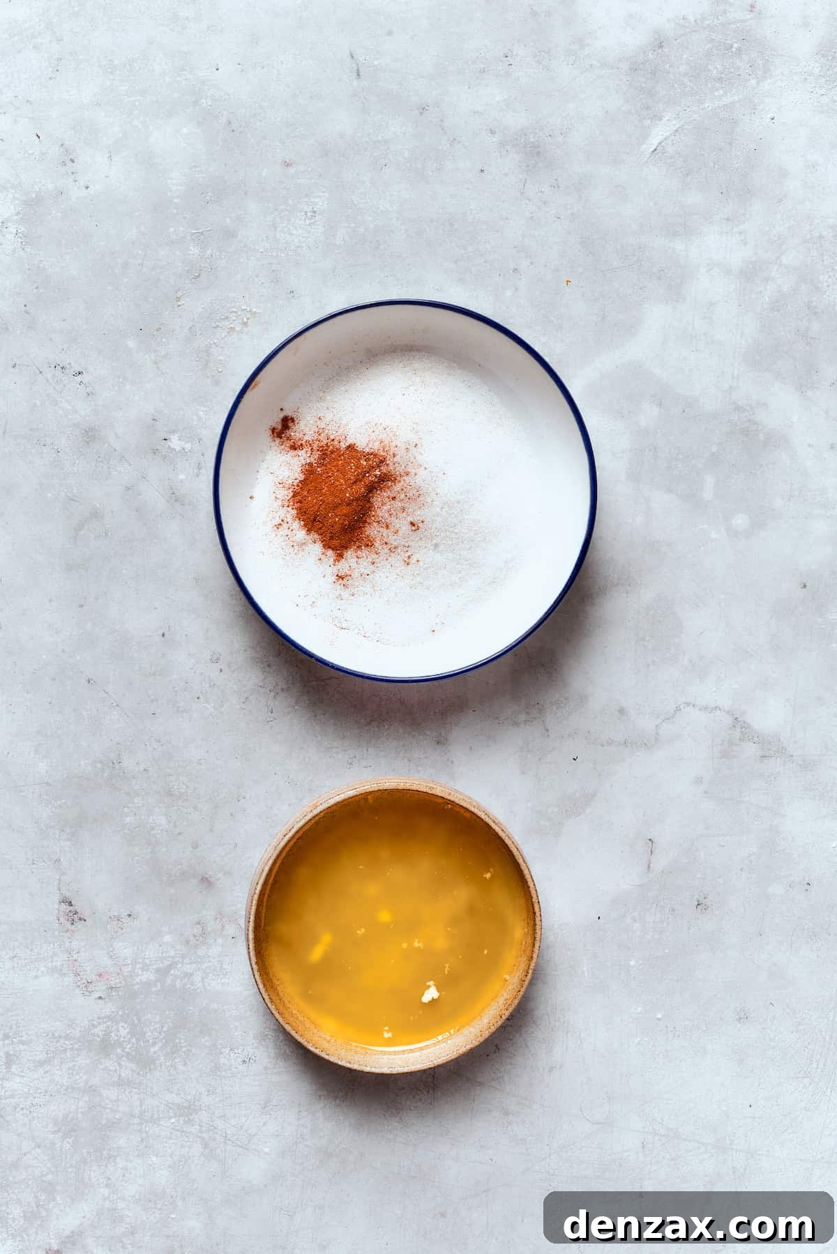 A shallow bowl holding melted butter and another bowl with the cinnamon-sugar topping, prepared for coating the baked donuts.
