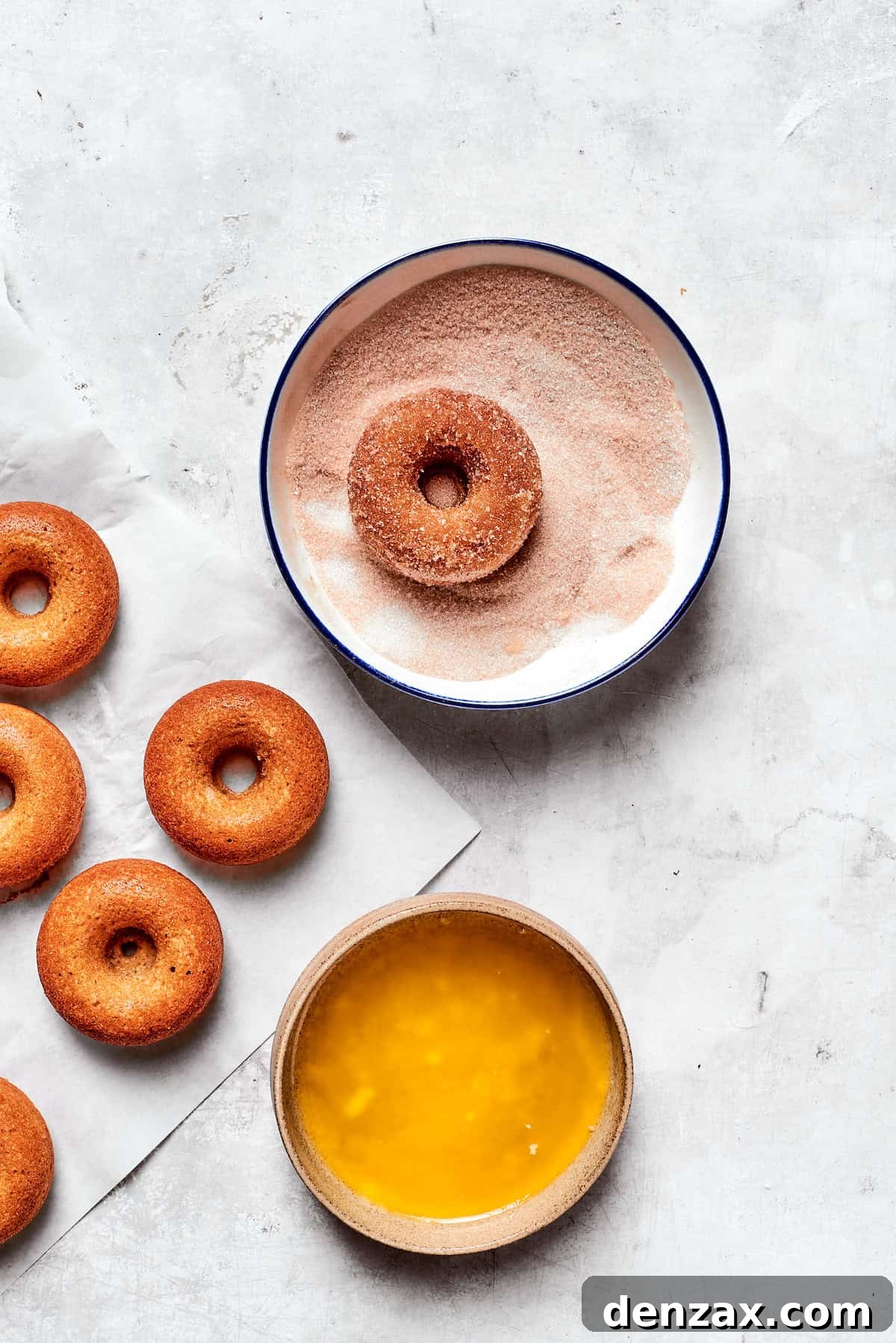 A freshly baked apple cider donut being dipped into a bowl of sparkling cinnamon sugar, ensuring a generous and even coating.