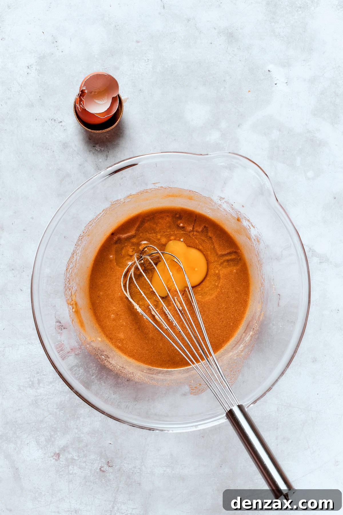 A large egg being whisked into the apple cider donut batter along with the reduced apple cider, creating a cohesive wet mixture.