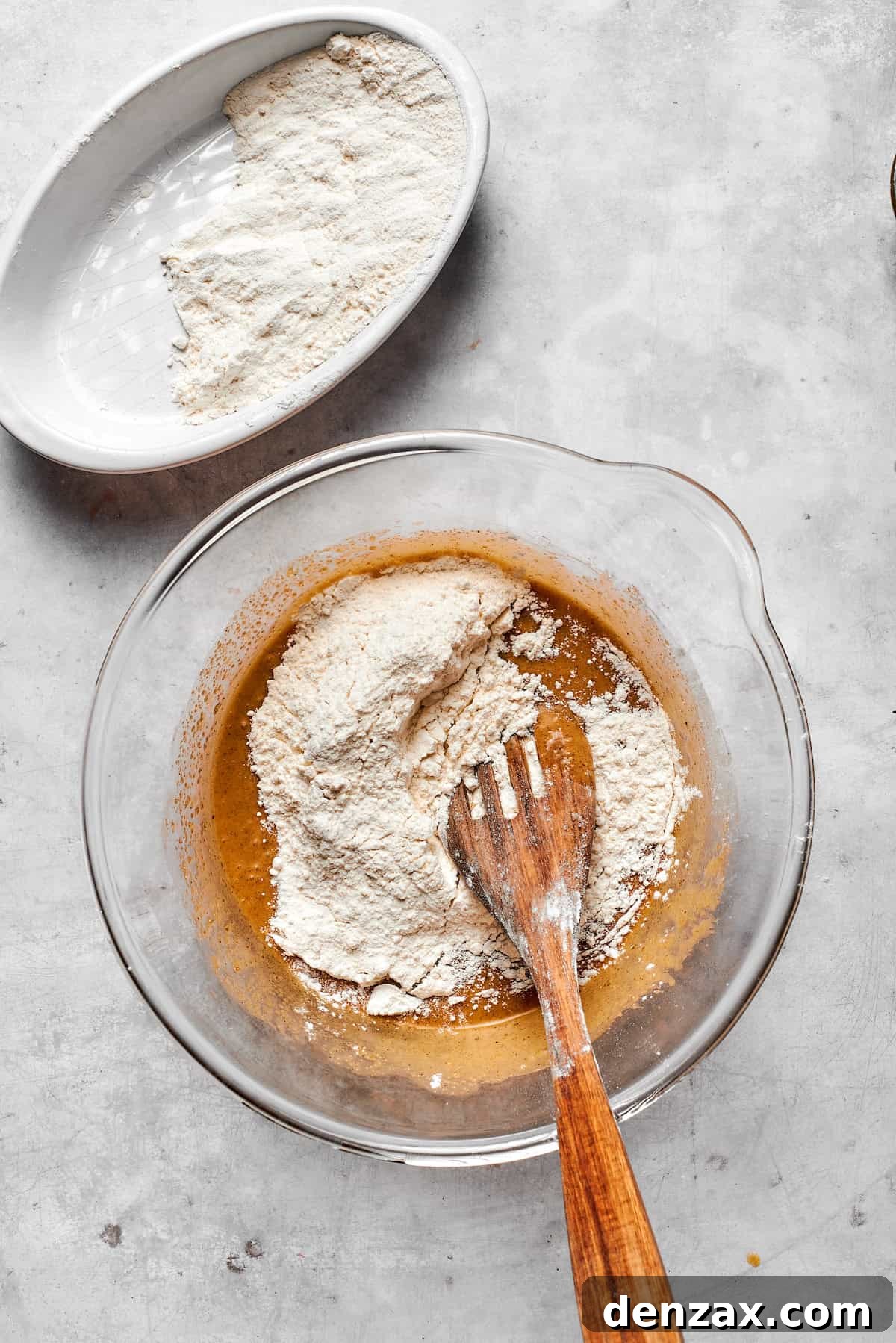 The pre-mixed dry ingredients are gradually folded into the wet cookie dough mixture using a spoon.