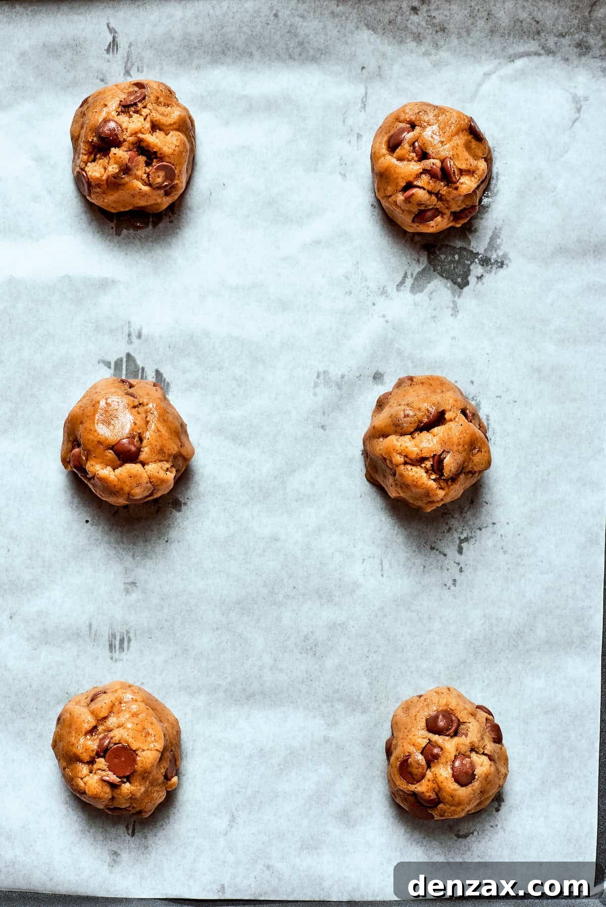 Uniform balls of brown butter chocolate chip cookie dough neatly arranged on a parchment-lined baking sheet, spaced for baking.