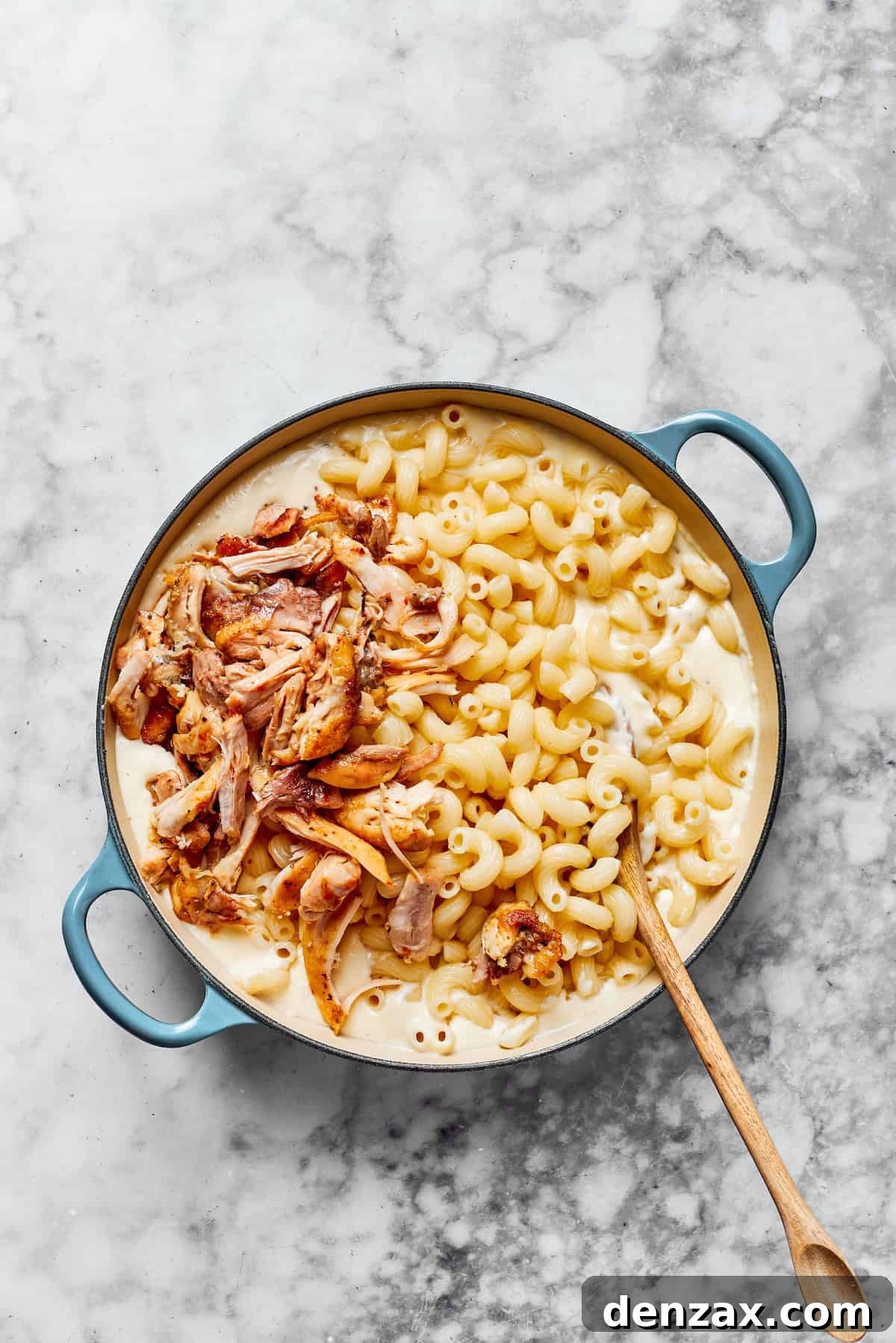 Cooked pasta and shredded chicken being folded into the creamy garlic Parmesan sauce in a large pan.
