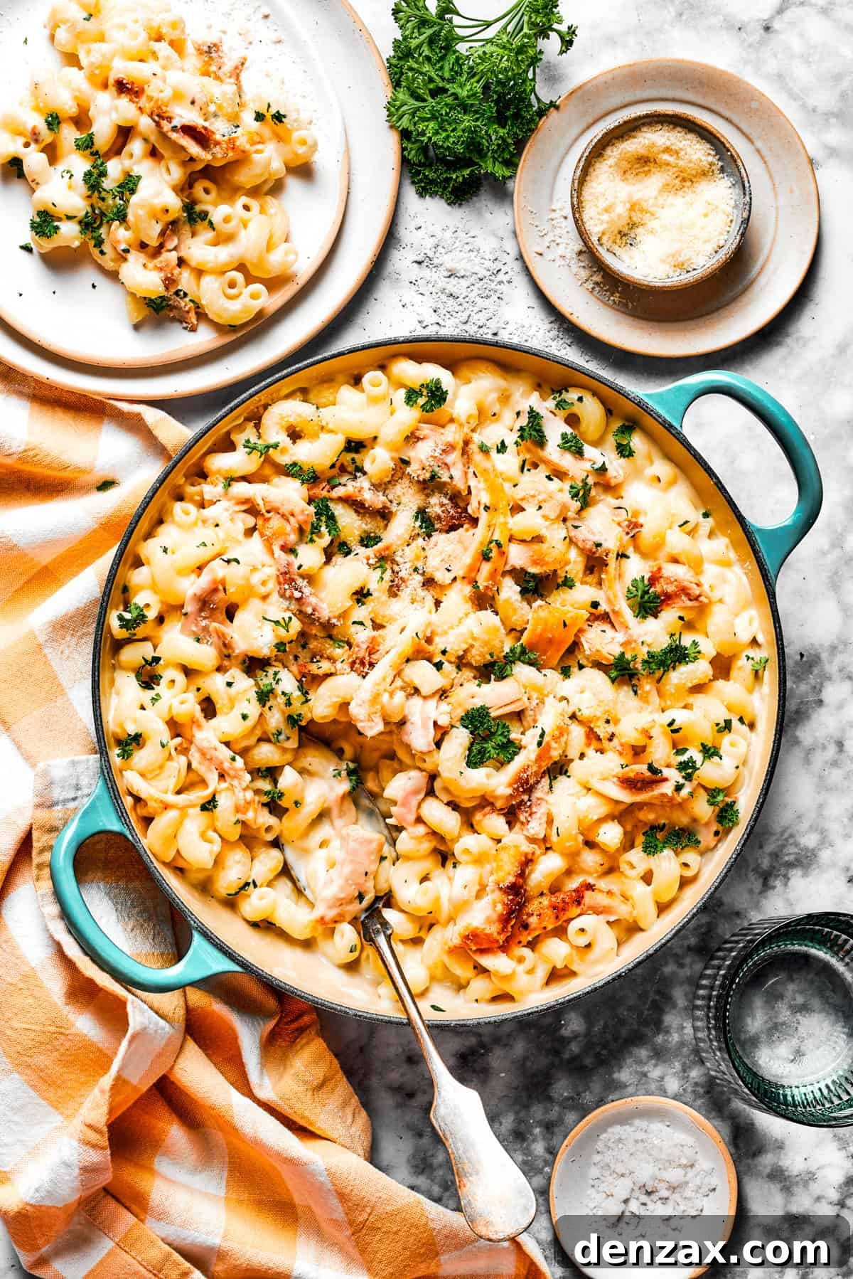 Overhead photo of a large pot filled with garlic parmesan chicken pasta, with a portion served on a white dinner plate next to it, garnished with parsley.