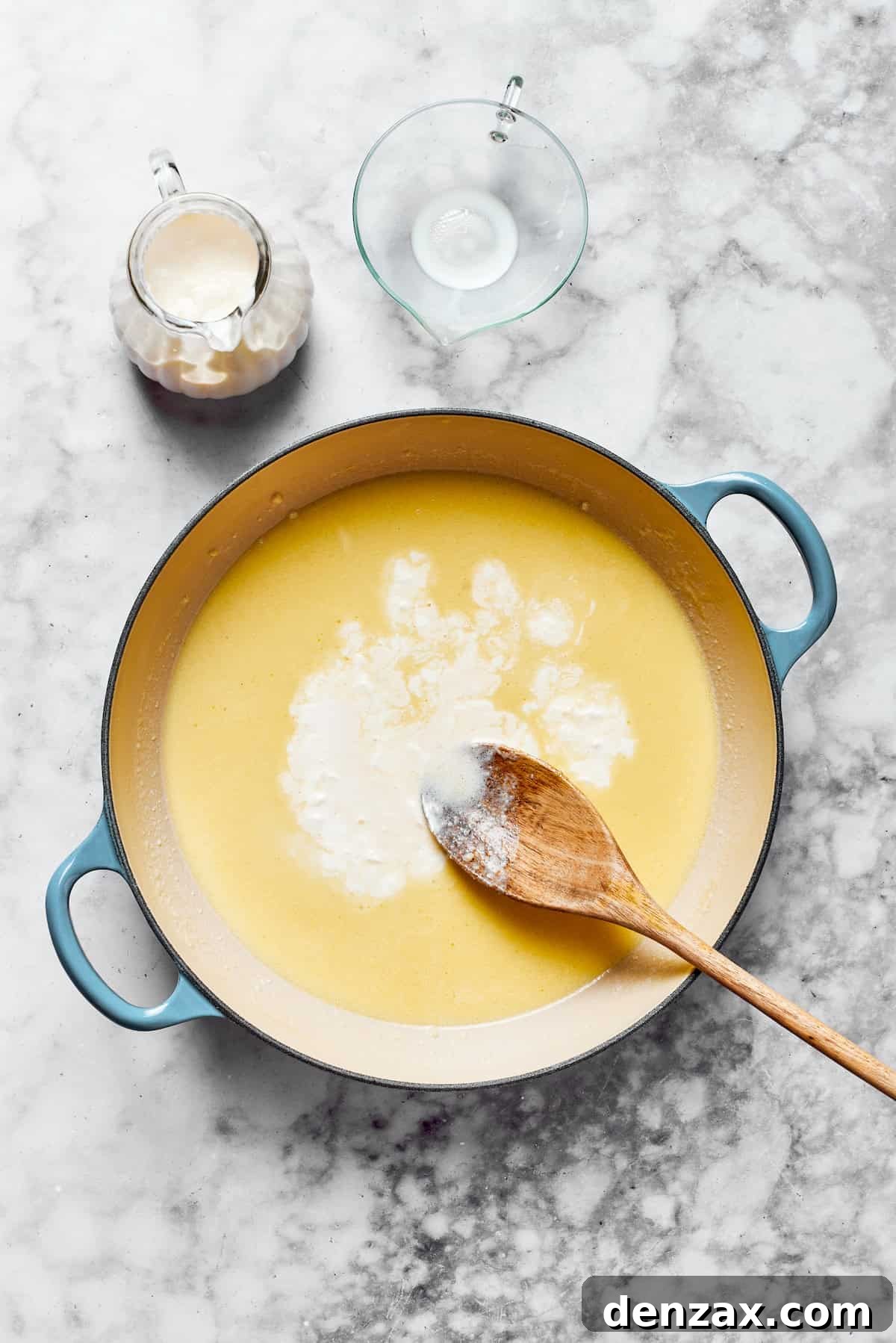 A creamy roux in a pan being combined with milk and heavy cream.