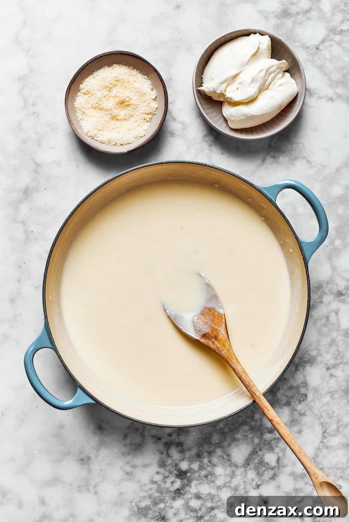 A smooth, creamy roux in a pan, with shredded Parmesan and cubed cream cheese nearby.