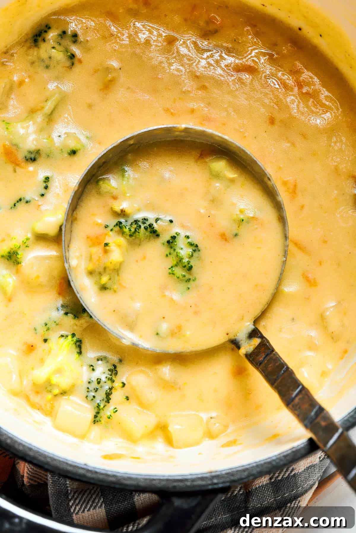 A ladle gracefully spooning out rich and creamy broccoli cheese soup from a large cooking pot, ready for serving.