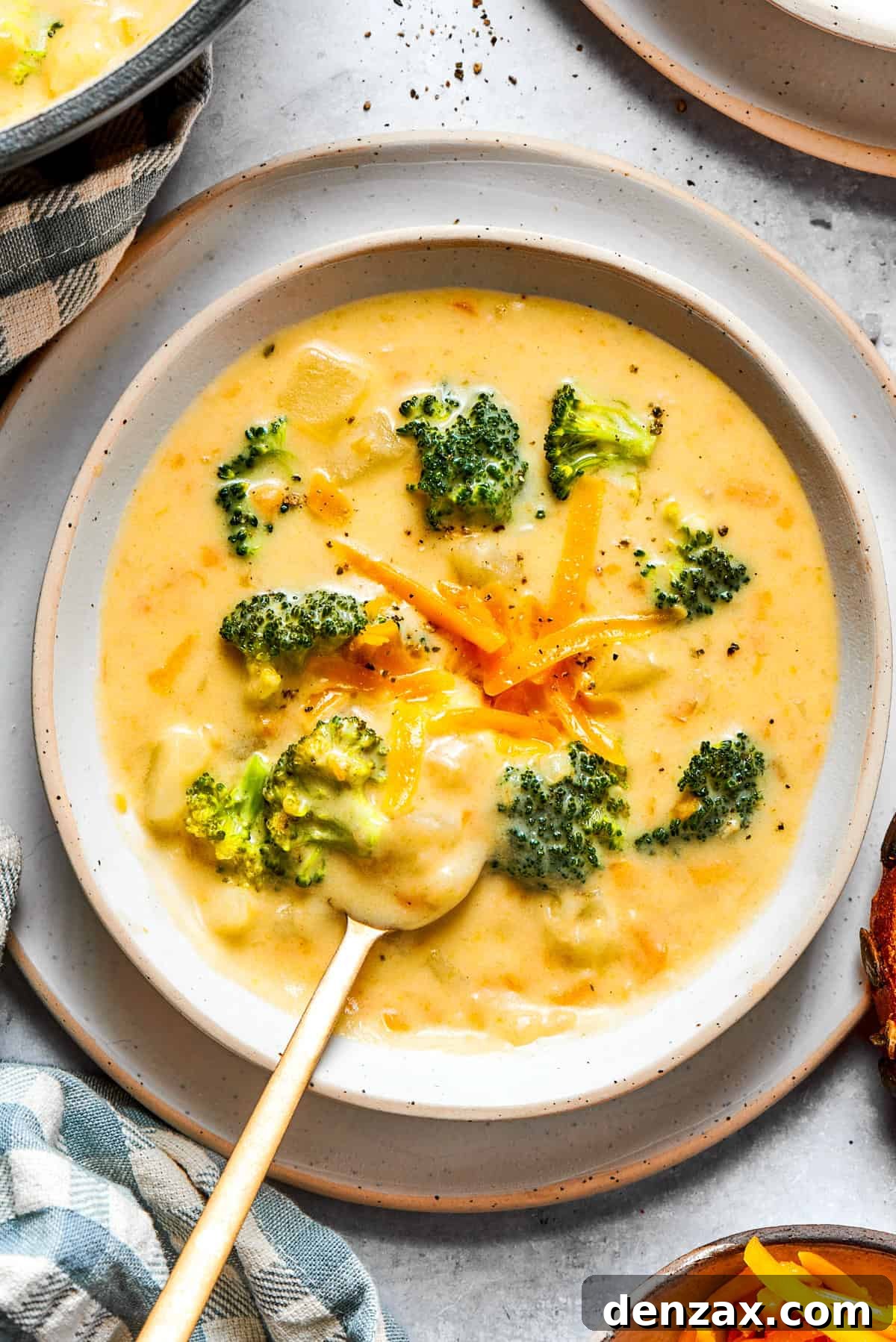 A beautifully garnished bowl of broccoli cheese soup, topped with a generous amount of shredded cheddar cheese and small fresh broccoli florets, showcasing its creamy texture.