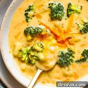 Bowl of broccoli cheese soup garnished with shredded cheese and broccoli florets.