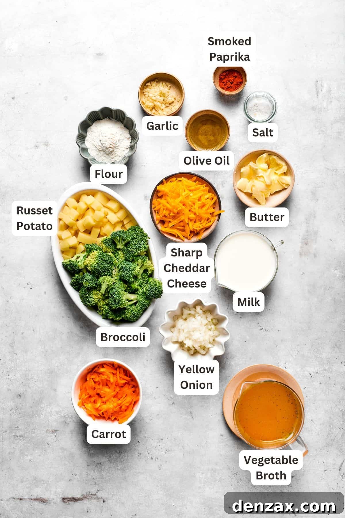 A curated selection of fresh ingredients for preparing homemade broccoli cheese soup, including broccoli florets, potatoes, carrots, onion, garlic, cheese, and broth.