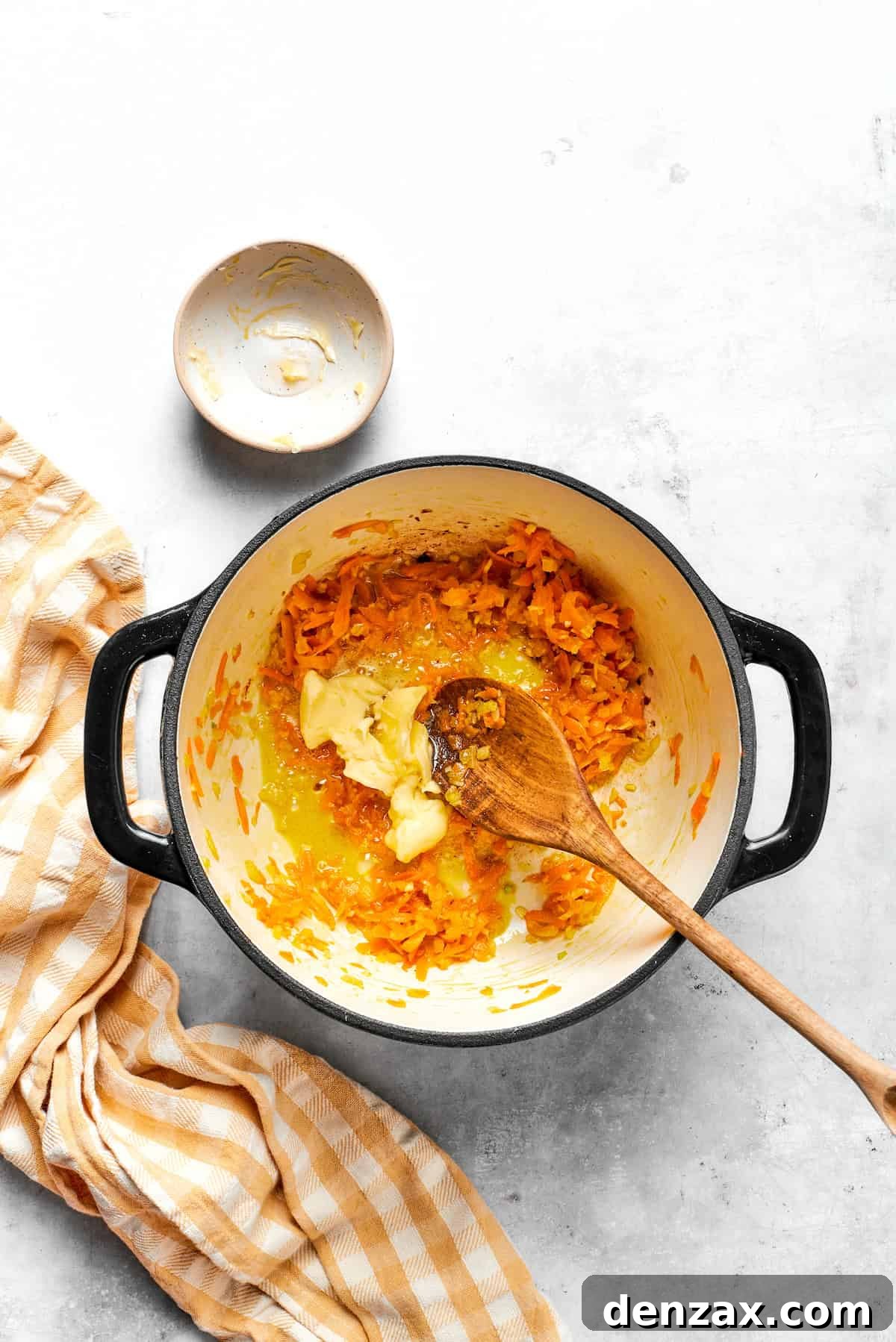 Adding unsalted butter to the softened carrots and onion in the soup pot, preparing to create the roux.