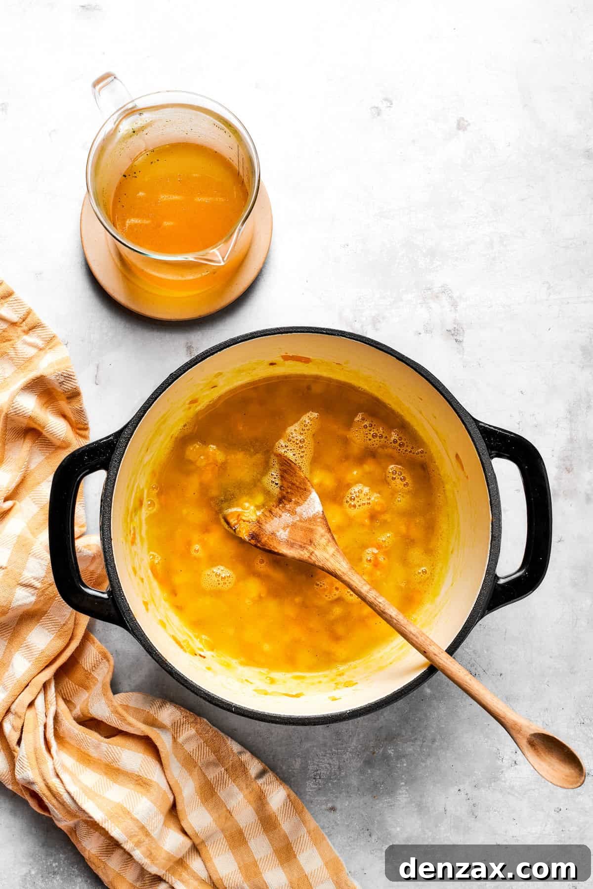 Slowly pouring vegetable broth into the roux and vegetables, whisking continuously to prevent lumps and create a smooth base.