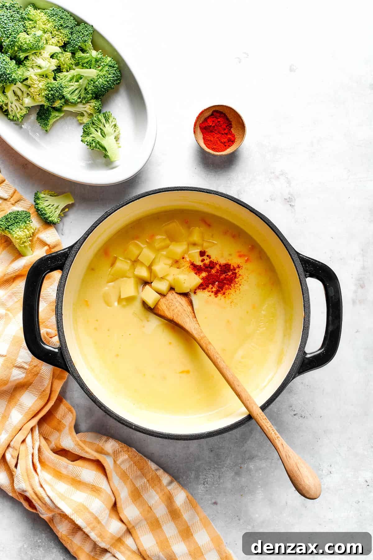 Adding bite-sized diced potatoes and a sprinkle of smoked paprika to the simmering soup, preparing for them to cook until tender.