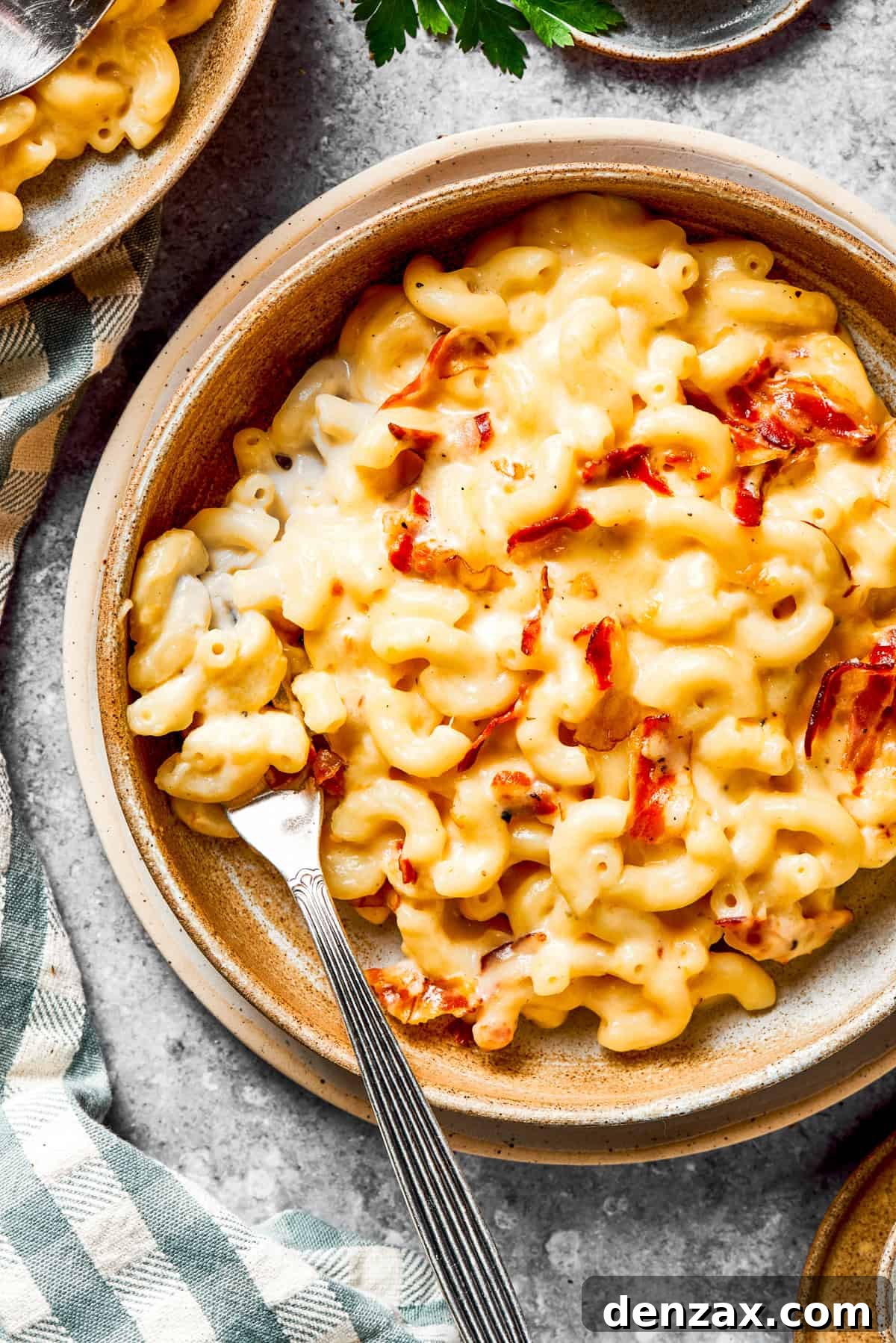 A single bowl of creamy bacon mac and cheese, garnished with a sprig of fresh herbs, with a fork resting inside.