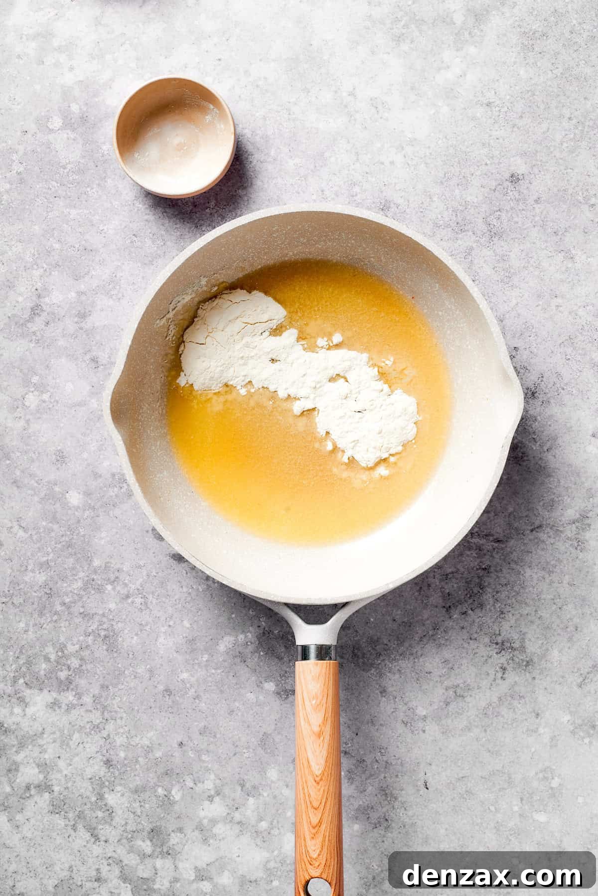 Melted butter in a skillet with flour being whisked in, forming a smooth roux, the base of the béchamel sauce.
