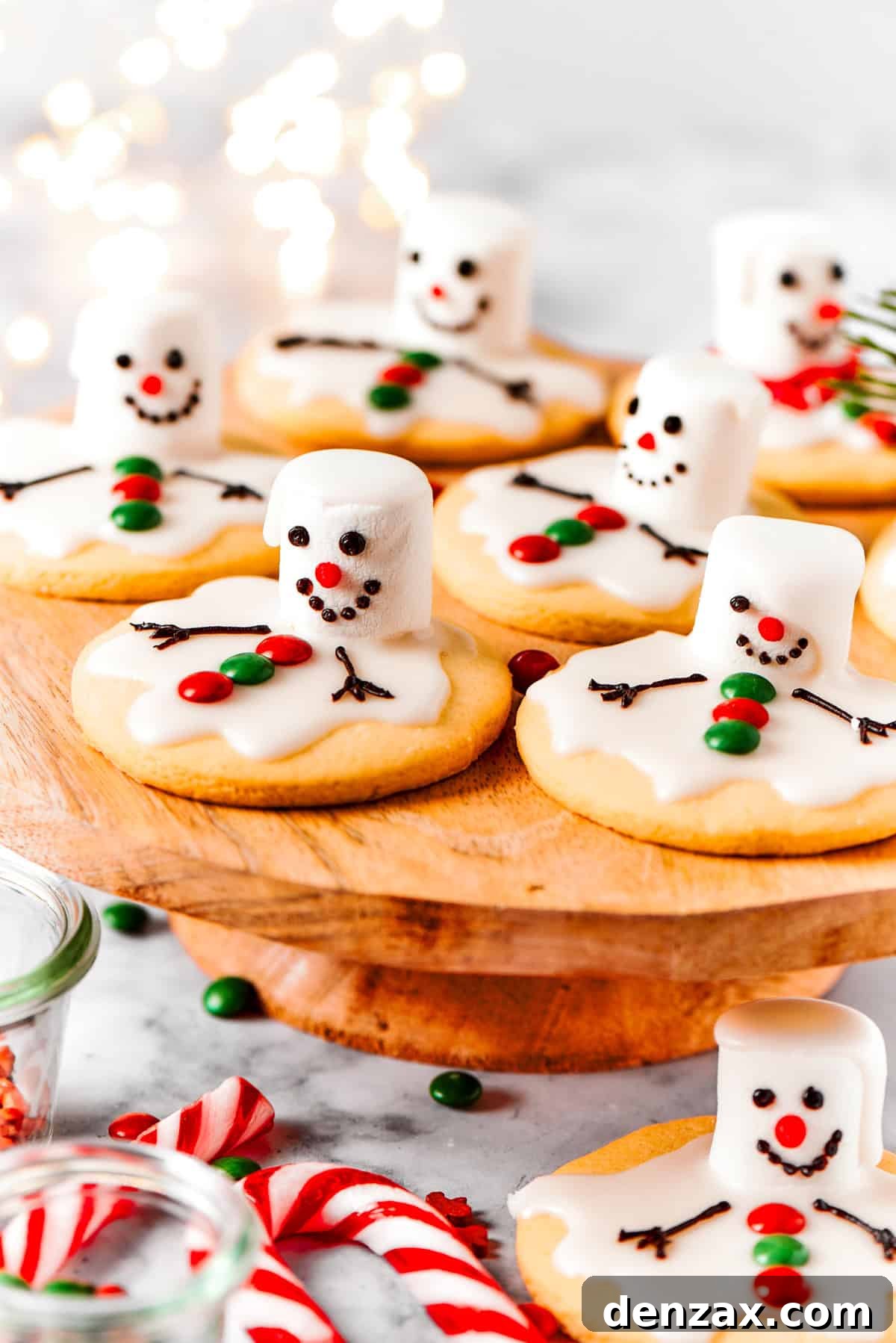 The cutest Melted Snowman Cookies top buttery homemade sugar cookies with a thick vanilla frosting and a fluffy marshmallow! Melting snowman cookies are arranged on a cake plate, showcasing their adorable, whimsical design.