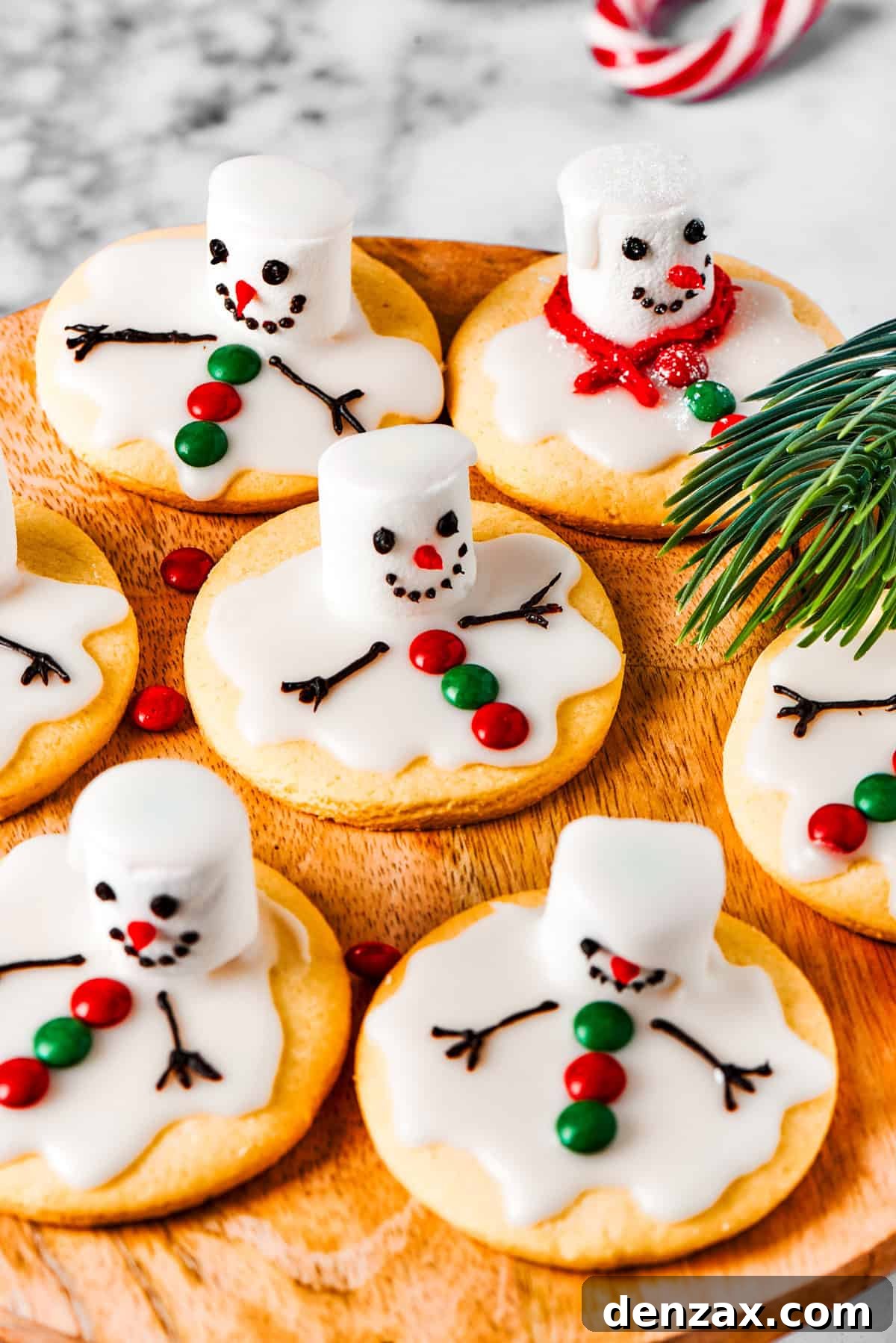 The cutest Melted Snowman Cookies top buttery homemade sugar cookies with a thick vanilla frosting and a fluffy marshmallow! A charming display of melted snowman cookies arranged neatly on a wooden tray, ready to be enjoyed.