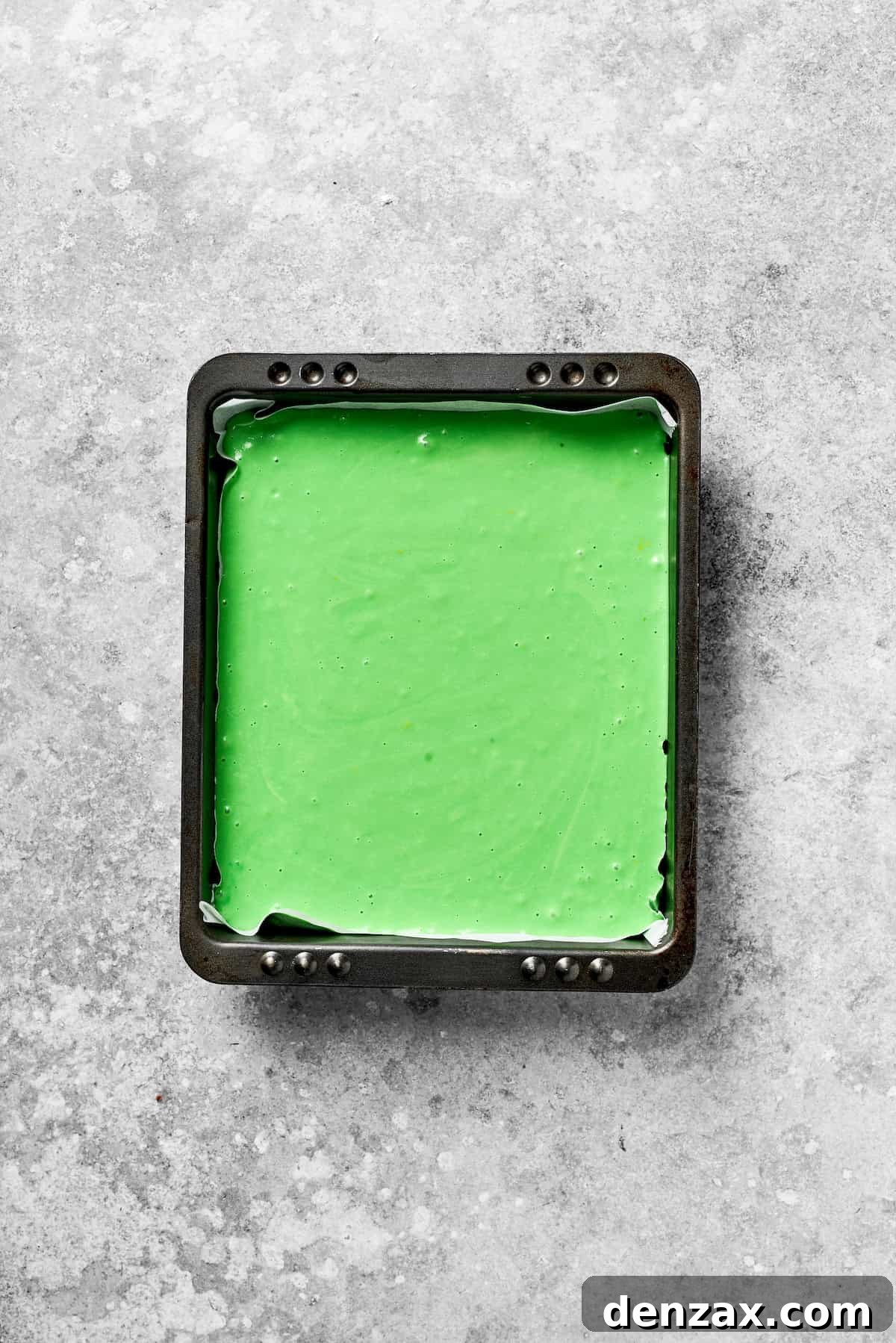 Green Grinch Cake Batter Poured into Baking Pan Vibrant green cake batter is poured into a greased square baking pan, ready for the oven.