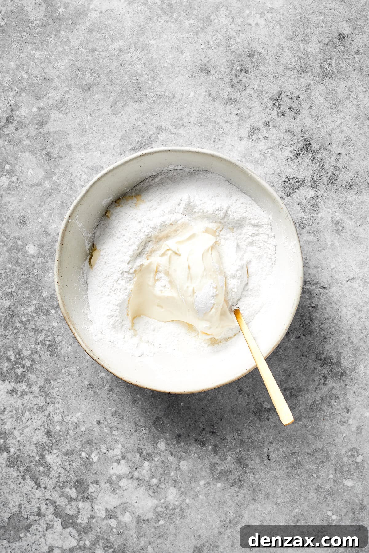 Mix Cream Cheese and Powdered Sugar for Grinch Frosting Cream cheese and sifted powdered sugar are mixed together in a bowl, forming a smooth frosting base.