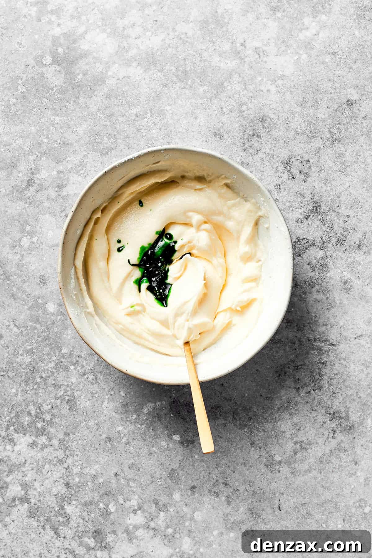 Add Green Food Coloring to Cream Cheese Frosting Green food coloring is squeezed into a bowl of creamy white icing, preparing for the Grinch transformation.
