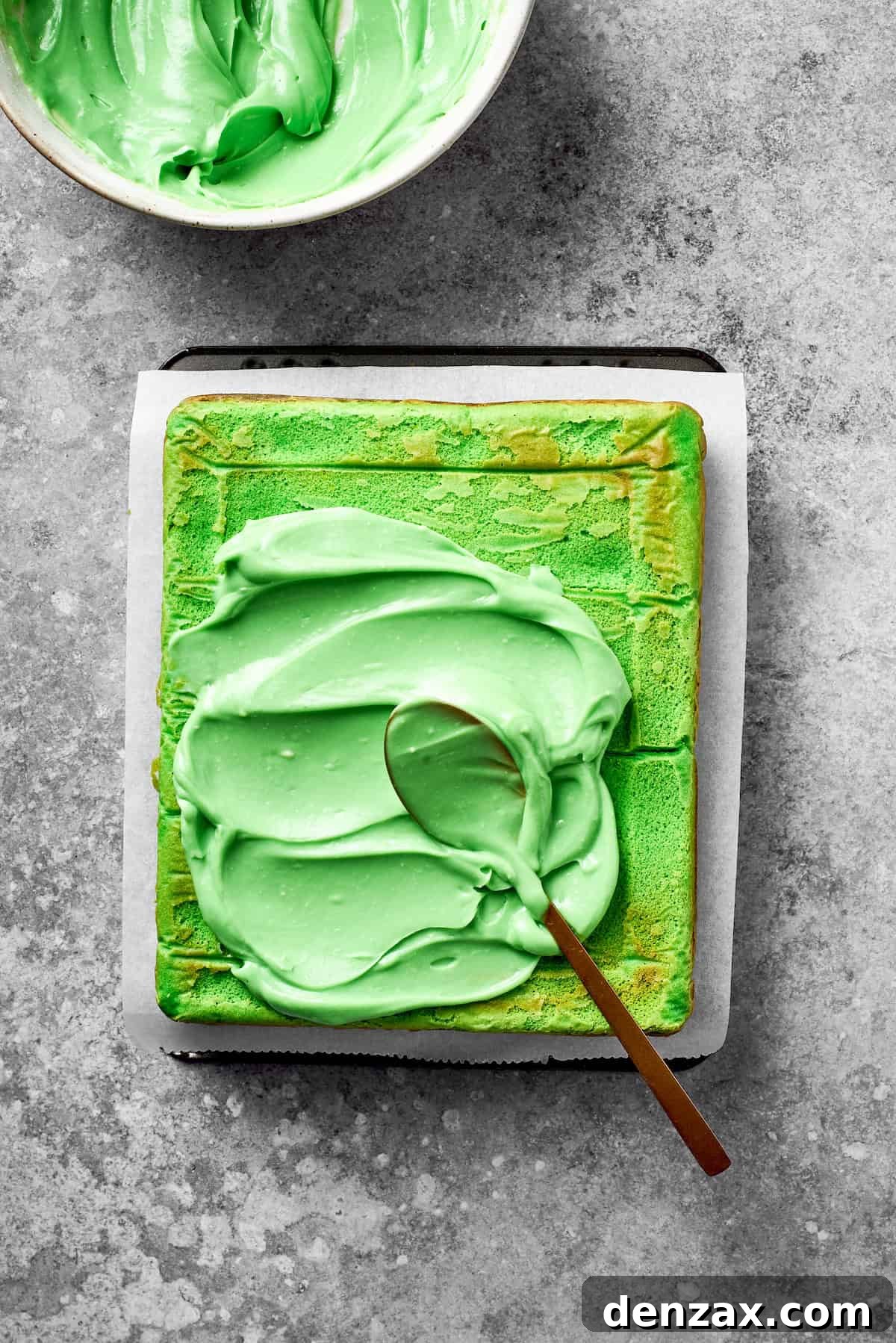 Apply Green Icing to the Baked Grinch Cake Vibrant green icing is generously spread across the top of a baked Grinch cake, preparing for decorations.