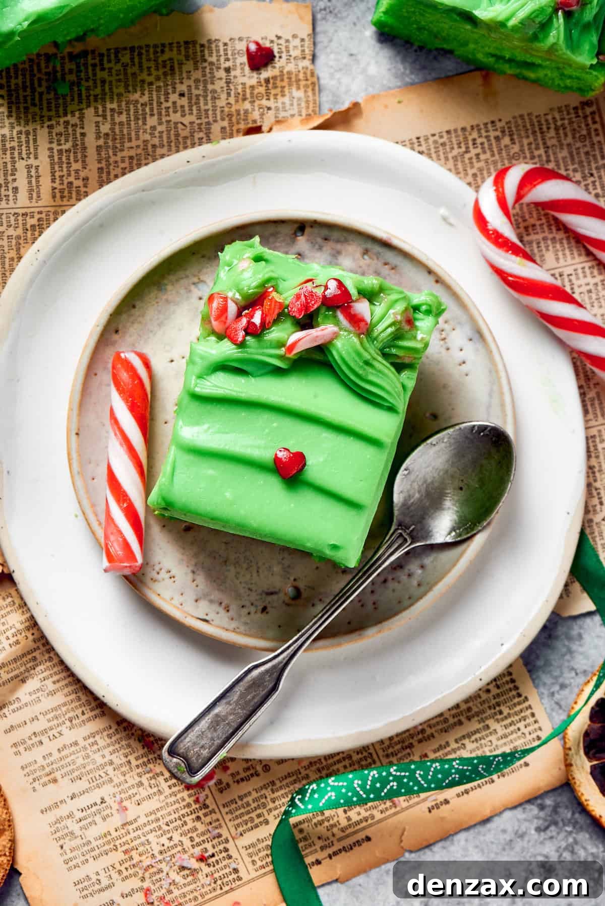 A Delicious Slice of Green Grinch Cake with a Spoon A beautifully plated slice of grinch cake, adorned with candies, sits next to a spoon, inviting enjoyment.