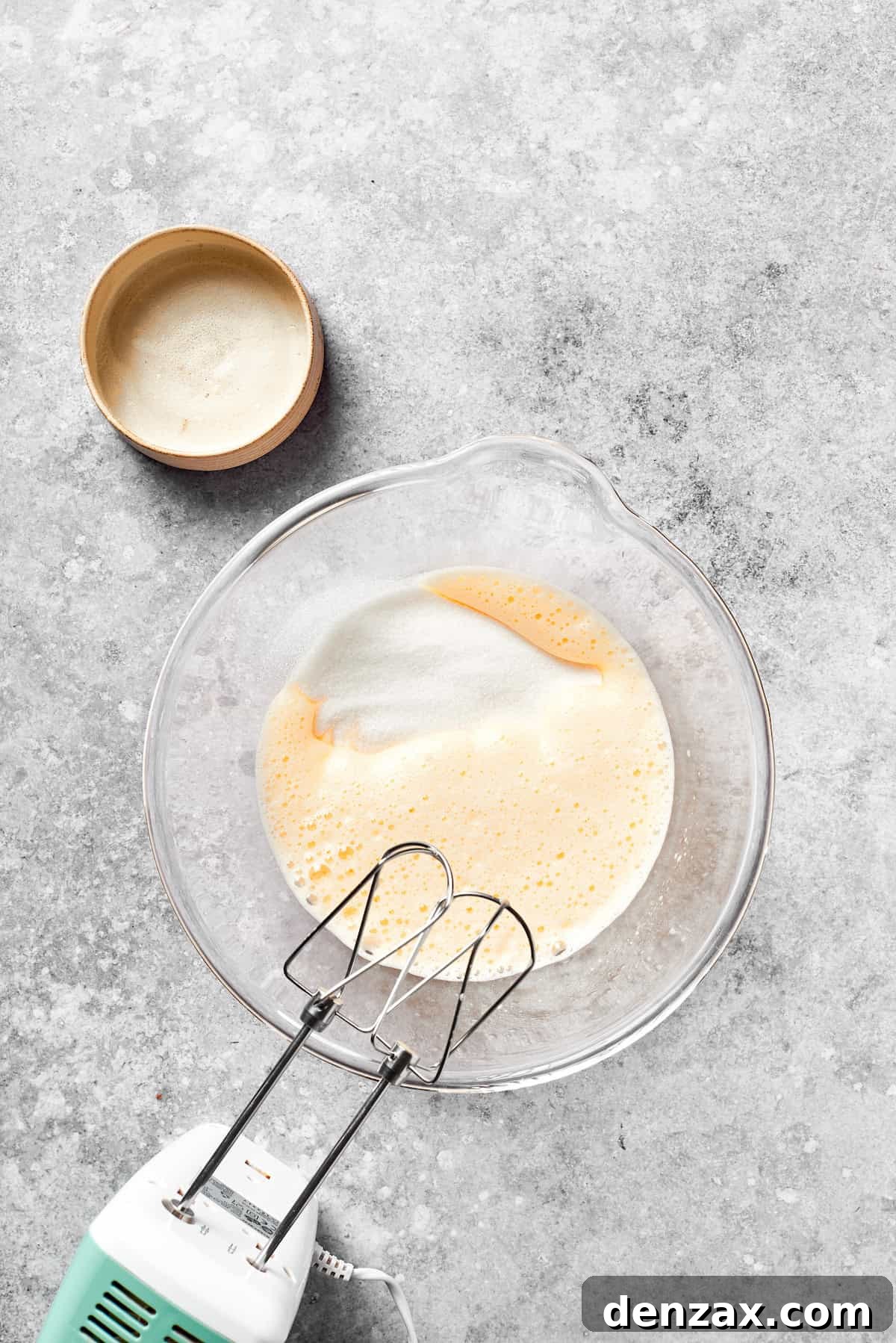 Incorporate Sugar into the Egg Mixture for Grinch Cake Granulated sugar being beaten into whisked eggs in a large mixing bowl, creating a smooth mixture.