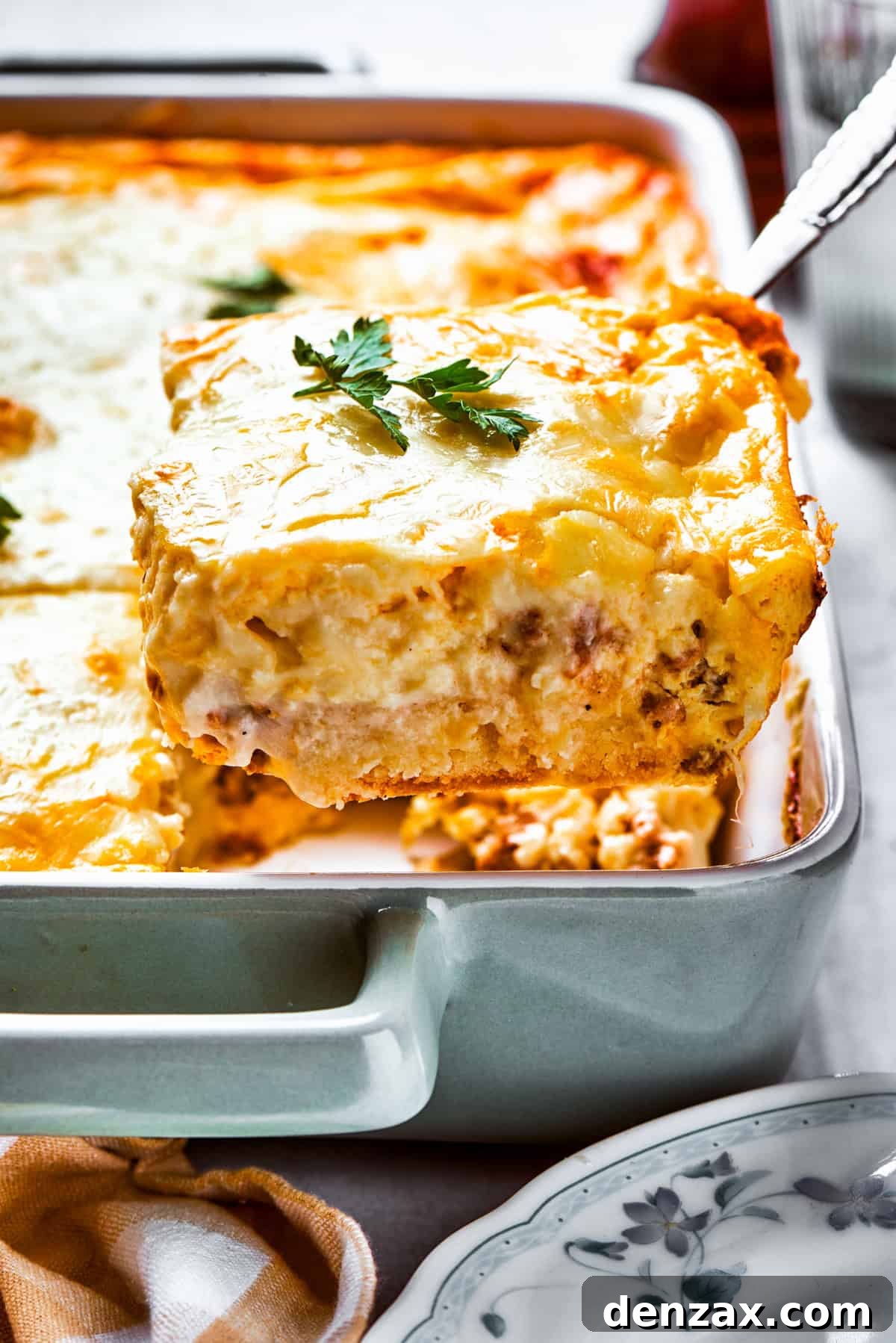 Lifting up a slice of biscuits and gravy casserole from a baking dish, showcasing its layers of flaky biscuit, creamy gravy, and melted cheese.