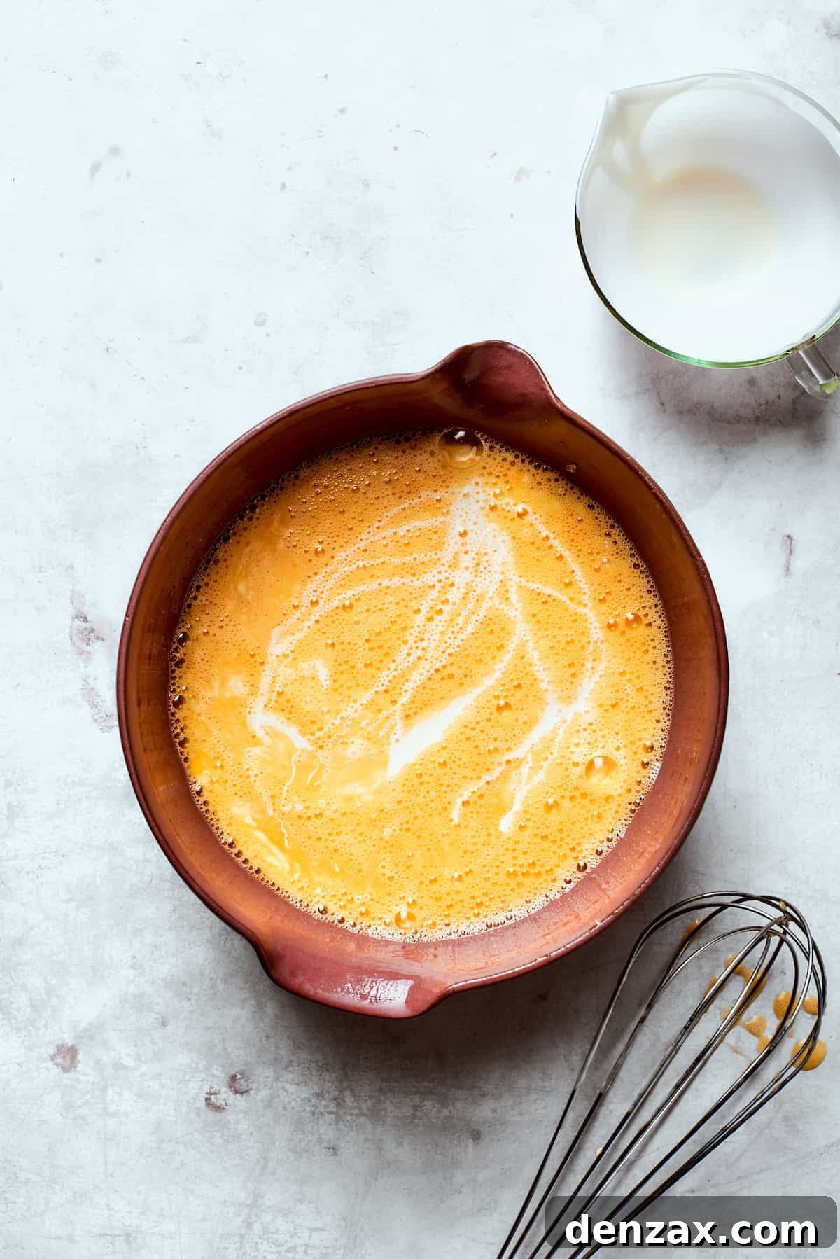 Eggs being whisked vigorously with heavy cream and salt in a mixing bowl.