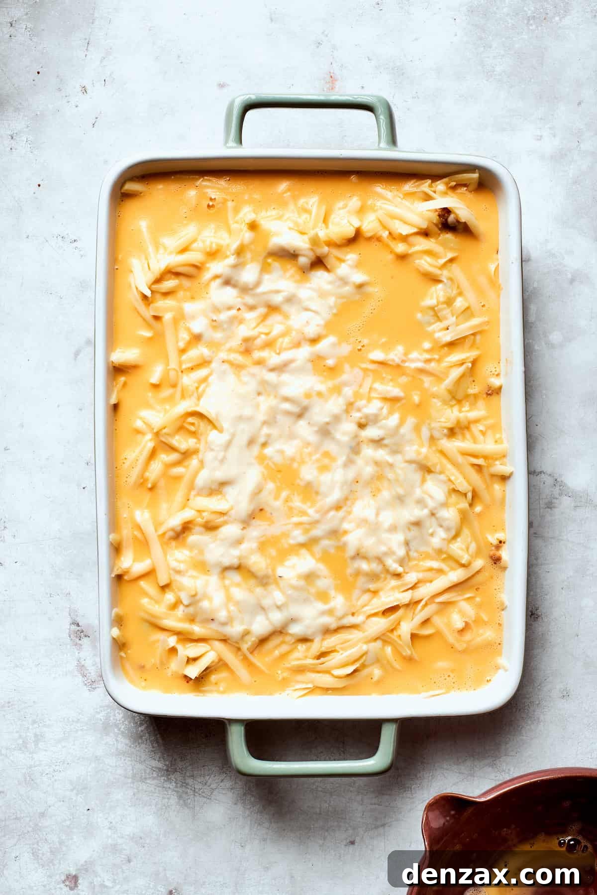 The whisked egg and cream mixture being poured over the cheese layer in the casserole dish.