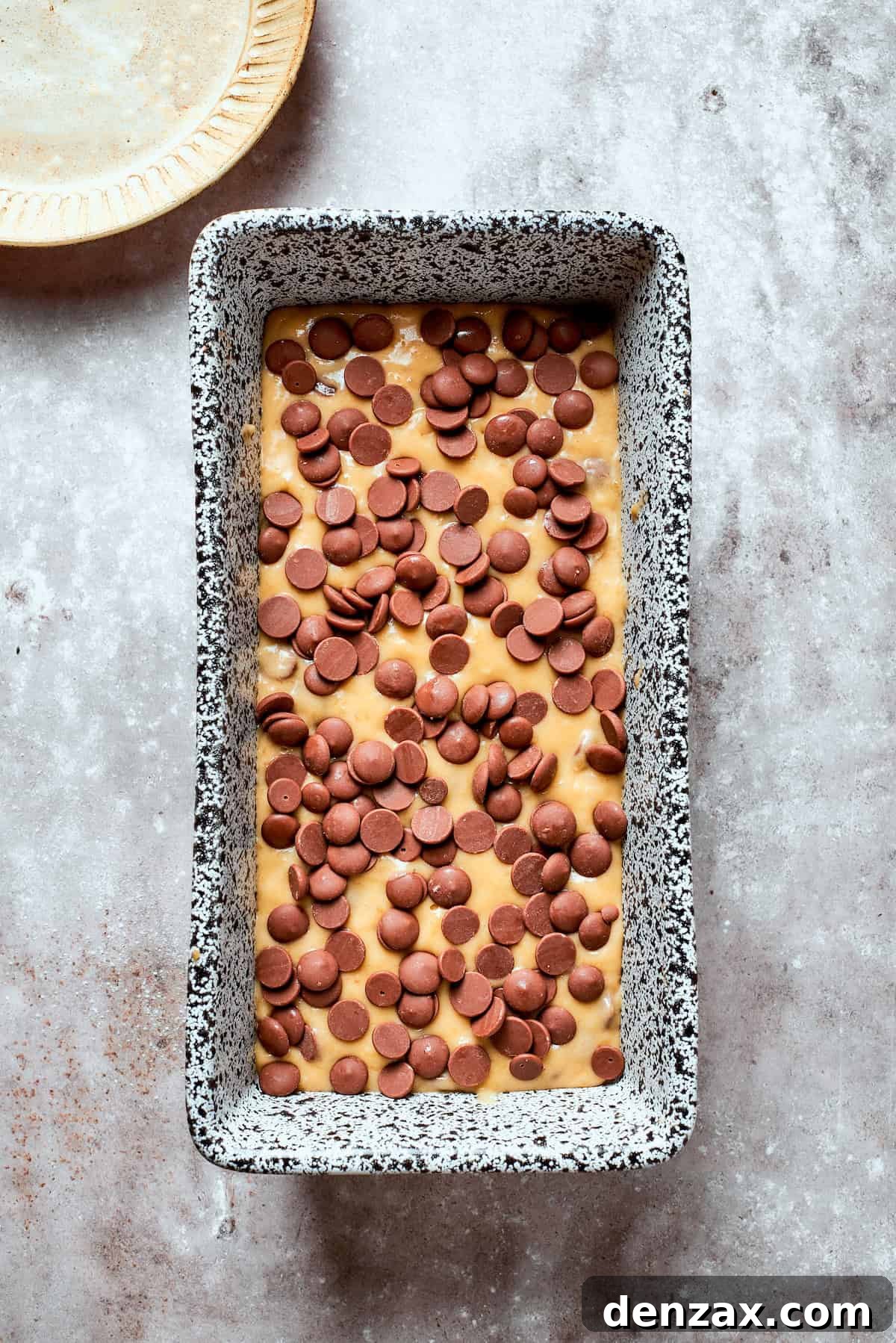 Banana chocolate chip bread batter poured into a loaf pan and topped with extra chocolate chips.