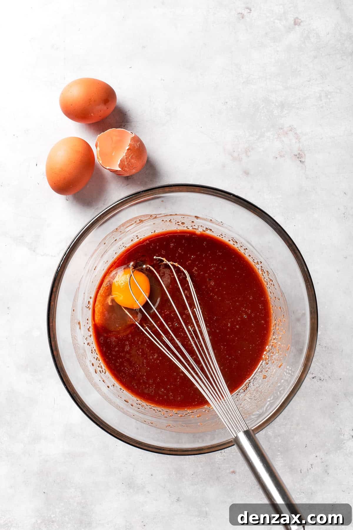 Large eggs are being cracked and added one by one into the chocolate mixture in a bowl, ready to be whisked.