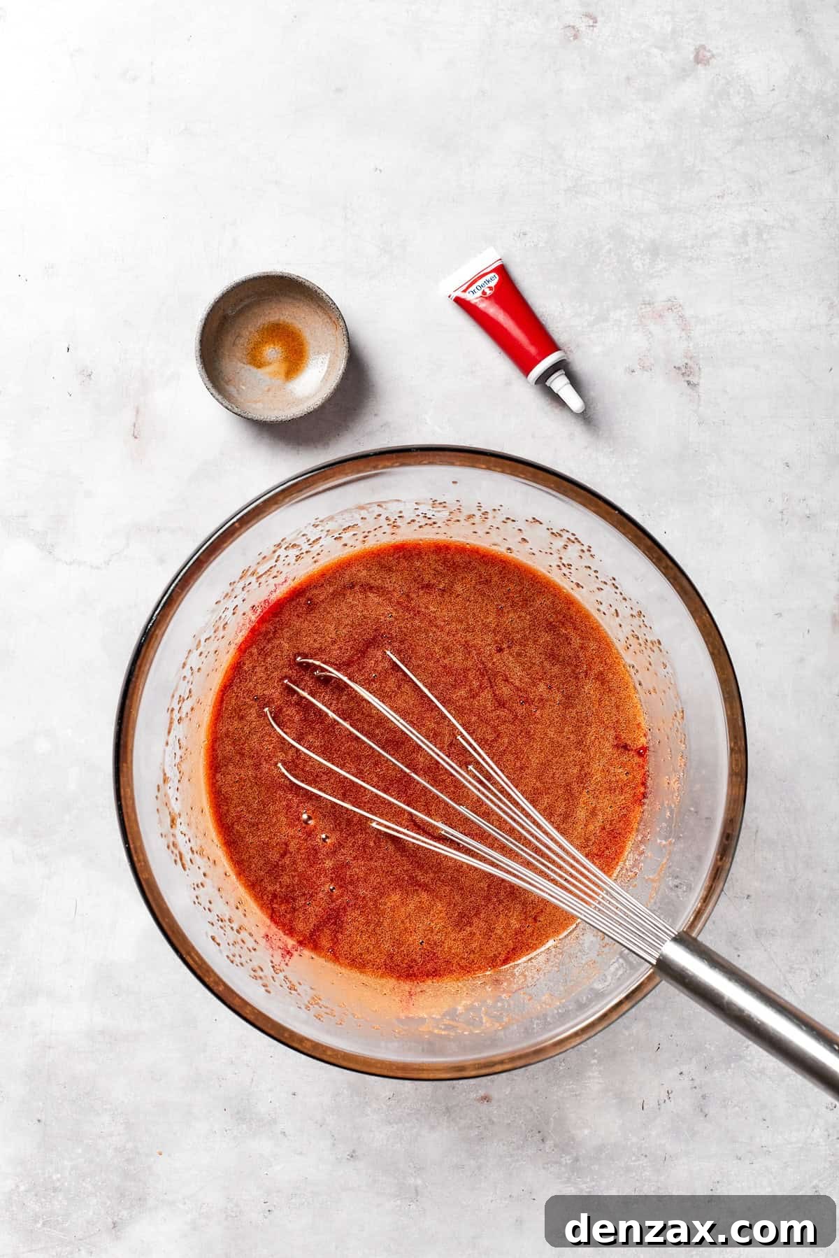 Pure vanilla extract is being poured into the red velvet brownie batter, enhancing its flavor.