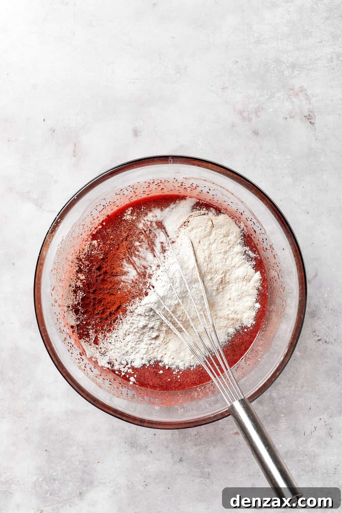 All-purpose flour is being sifted into the red velvet brownie batter in a mixing bowl.
