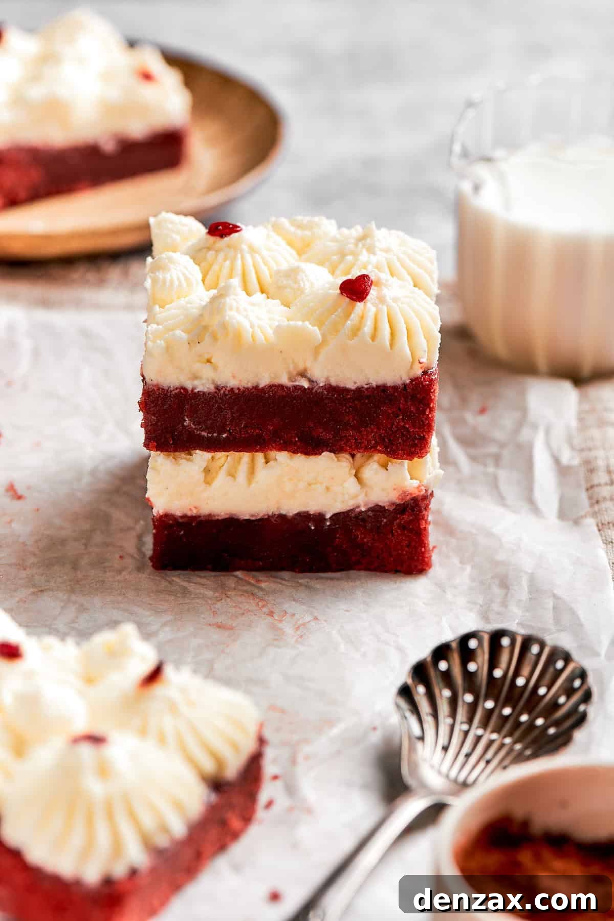 Two red velvet brownies, each adorned with a swirl of cream cheese frosting, are stacked neatly on top of one another.