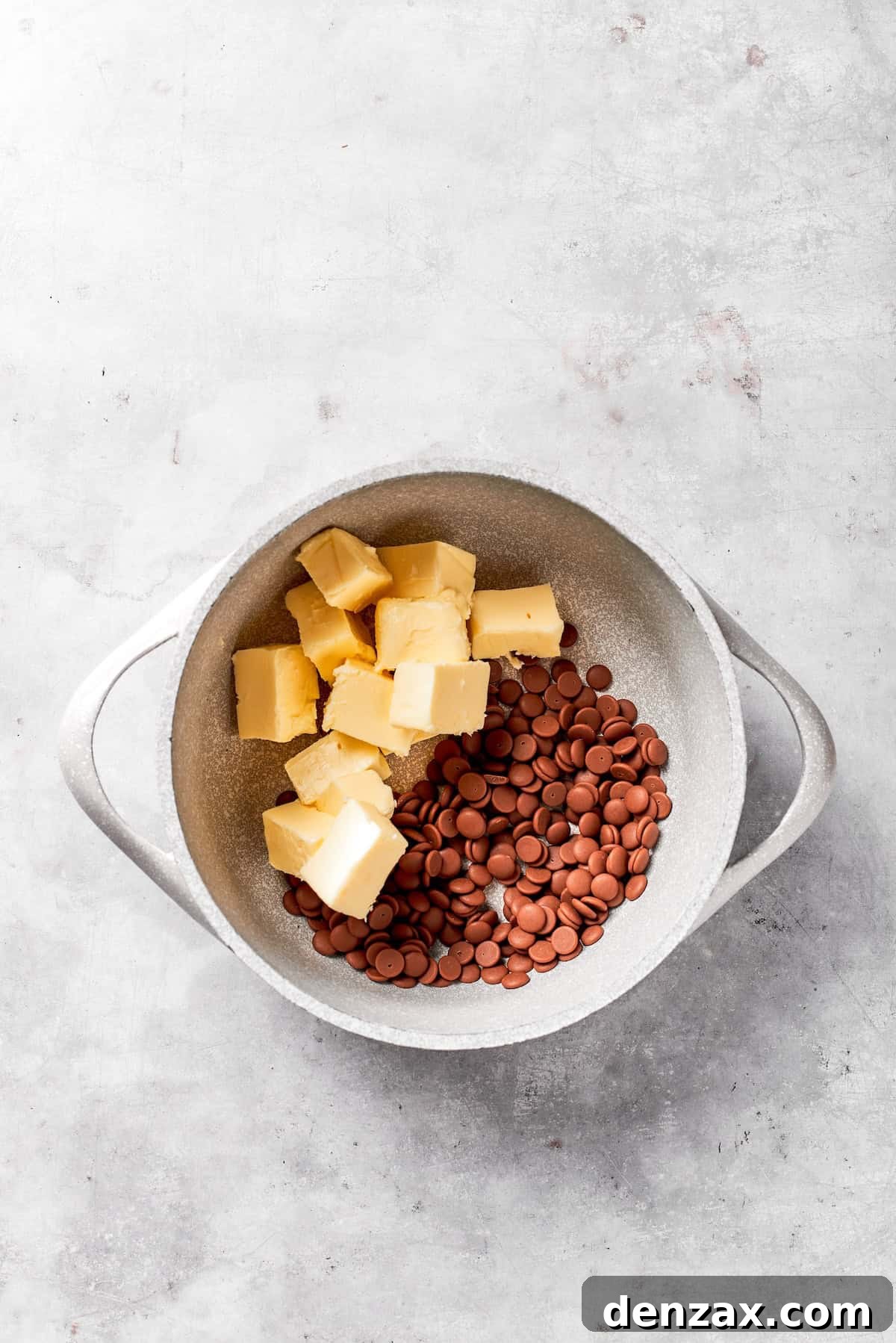 Cubes of unsalted butter are being added to a saucepan on a stovetop, ready to be melted.
