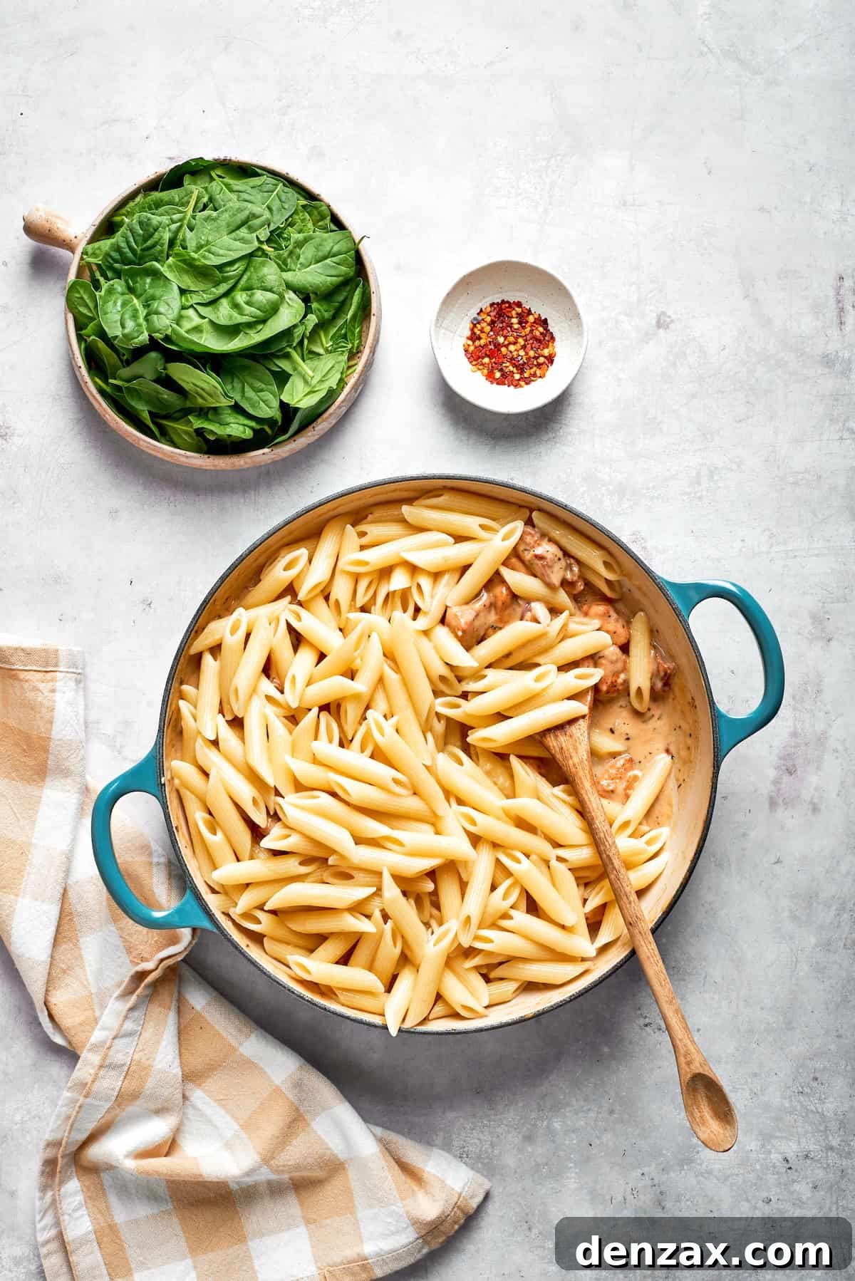 Pasta is stirred into cream sauce in a skillet.