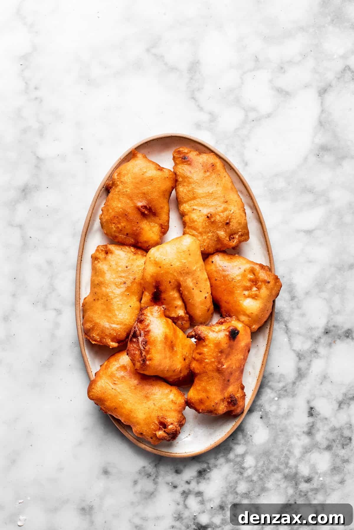 Freshly fried, golden-brown fish pieces resting on a plate, perfectly crispy and ready for sandwich assembly.