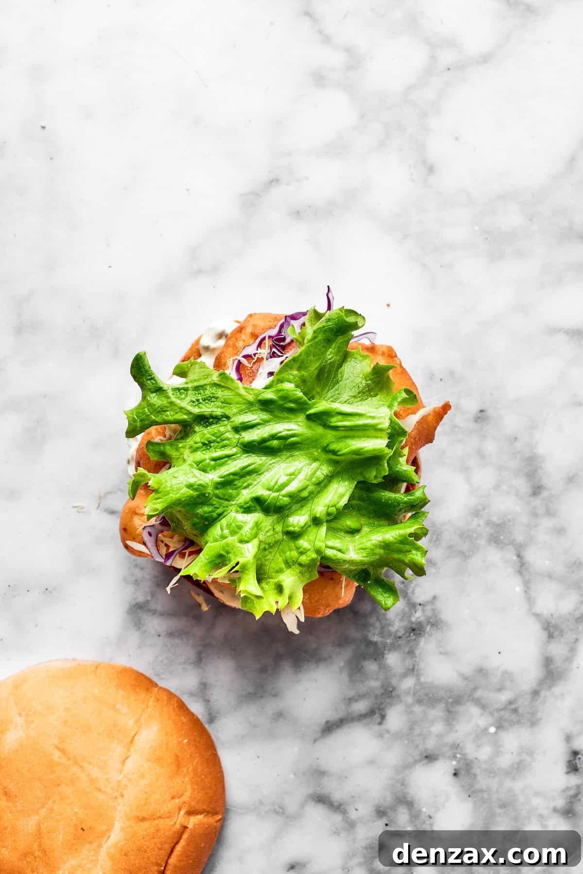A vibrant mix of shredded red and green cabbage being added on top of the fried fish fillet in a sandwich.