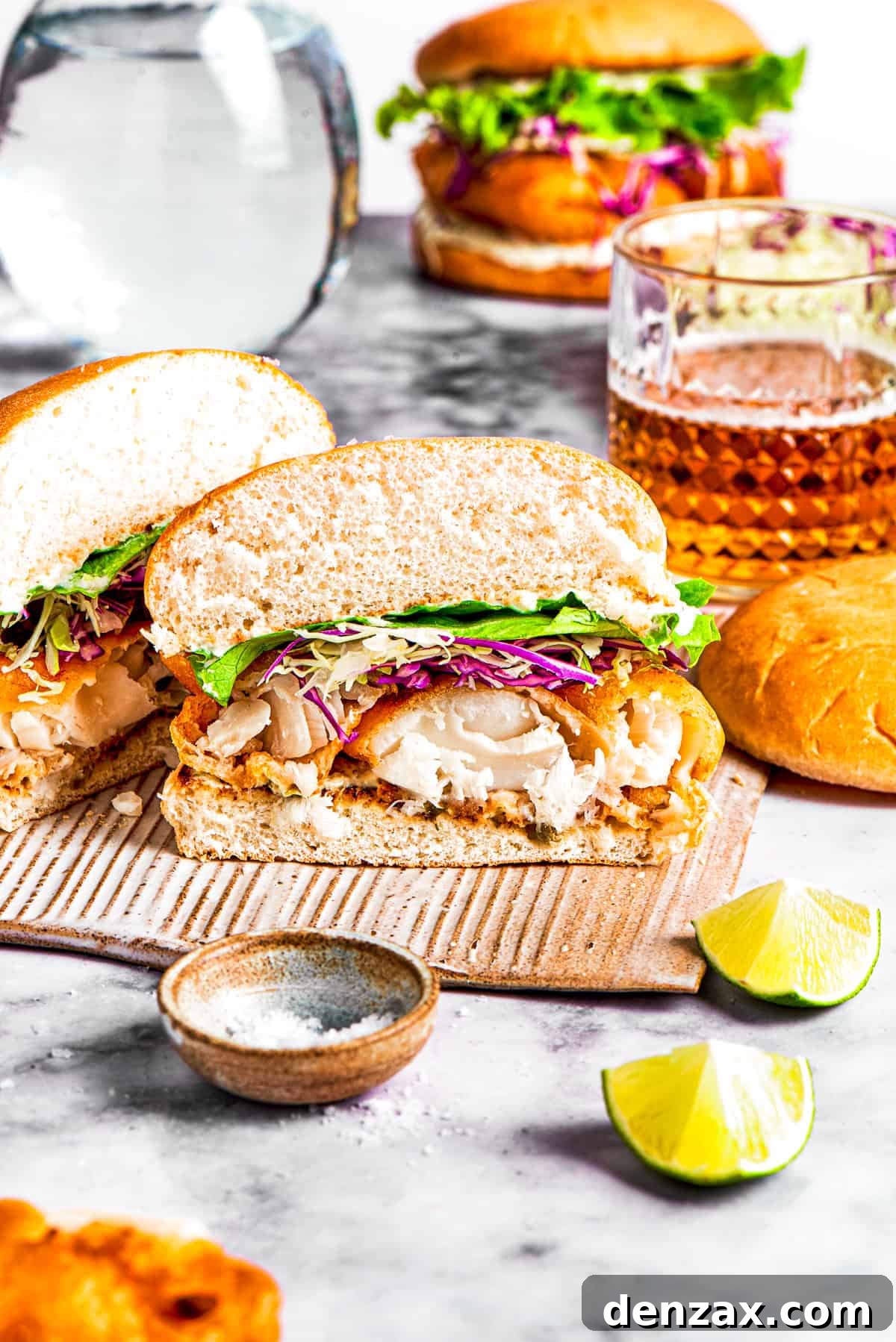 A perfectly assembled fish sandwich, cut in half to reveal the golden-fried fish, crisp lettuce, and shredded cabbage inside, ready to be enjoyed.