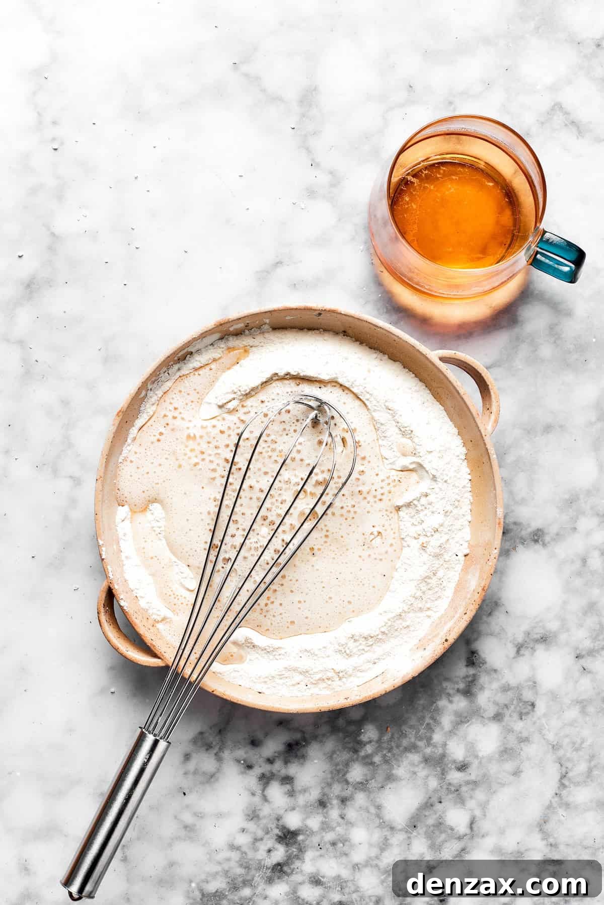 A whisk vigorously stirs a bowl of smooth, light golden beer batter, ready for dipping the fish.