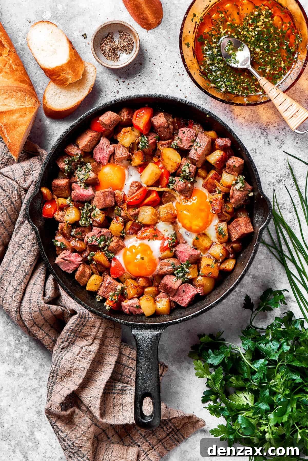 The finished cast iron skillet of steak and eggs, with perfectly fried eggs, resting on a kitchen towel with fresh herbs beside it.