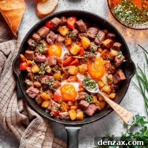 A cast iron skillet full of steak and eggs hash, with a spoon resting on the side, ready for serving.