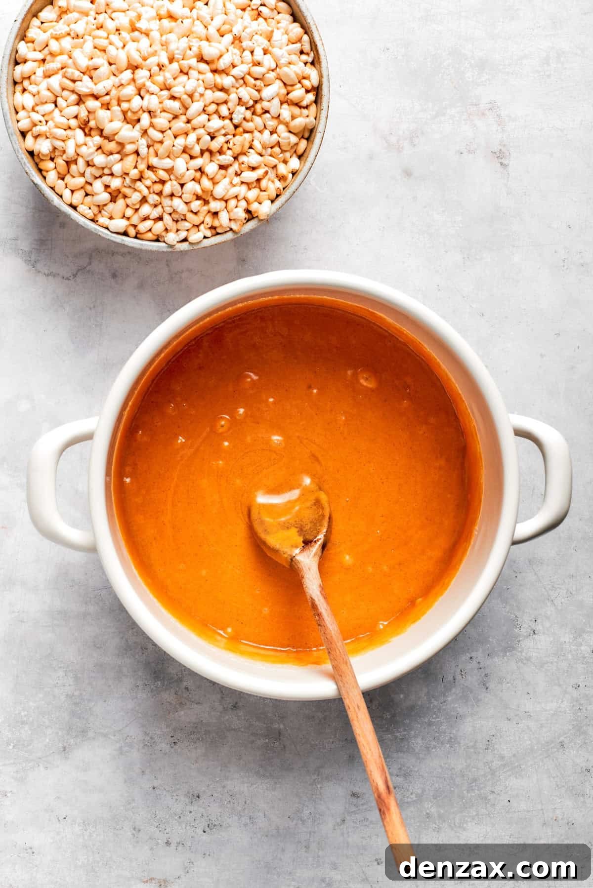 Creamy peanut butter is stirred into the warm honey and sugar mixture in a pot.