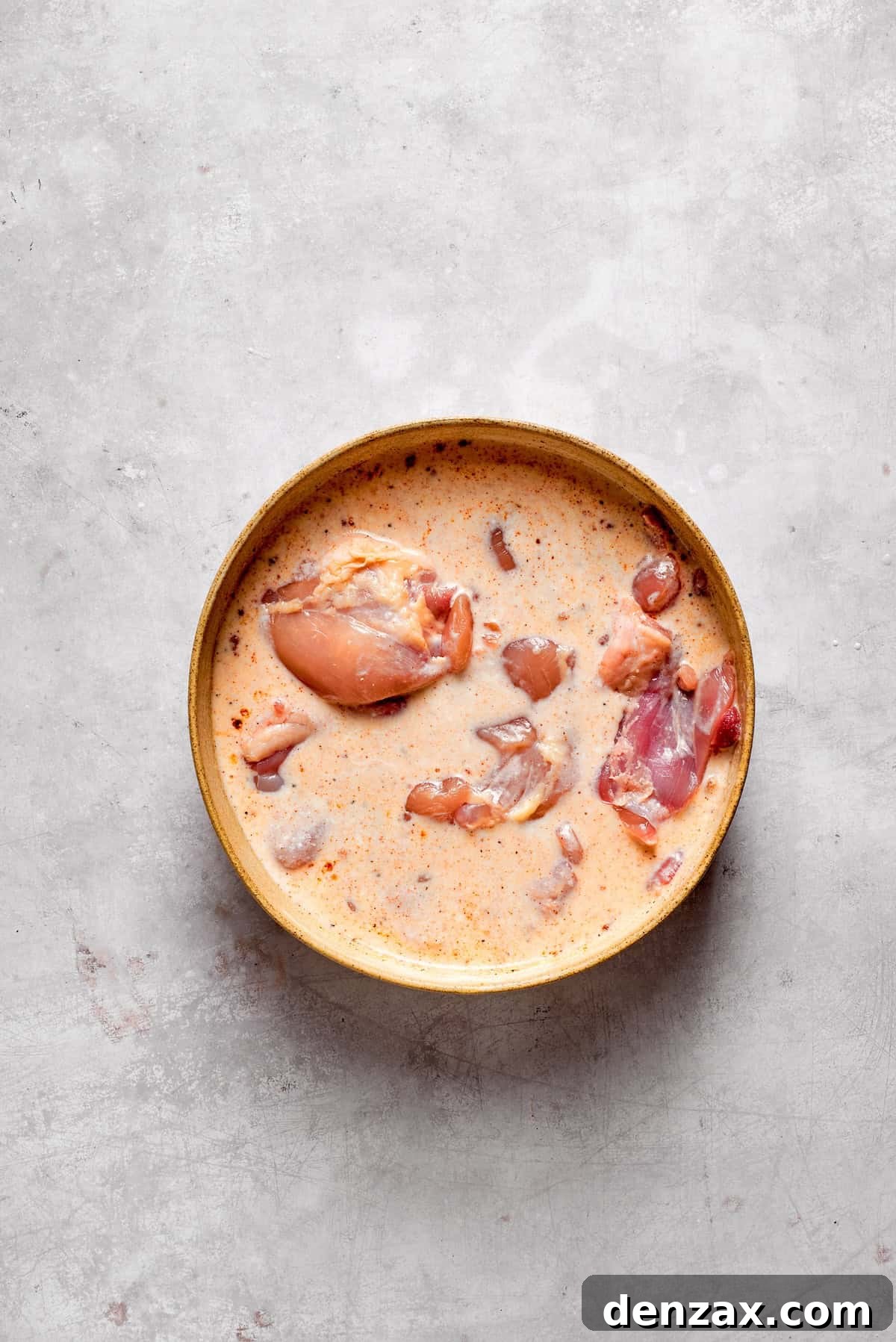 Boneless chicken thighs soaking in a rich buttermilk marinade within a mixing bowl.