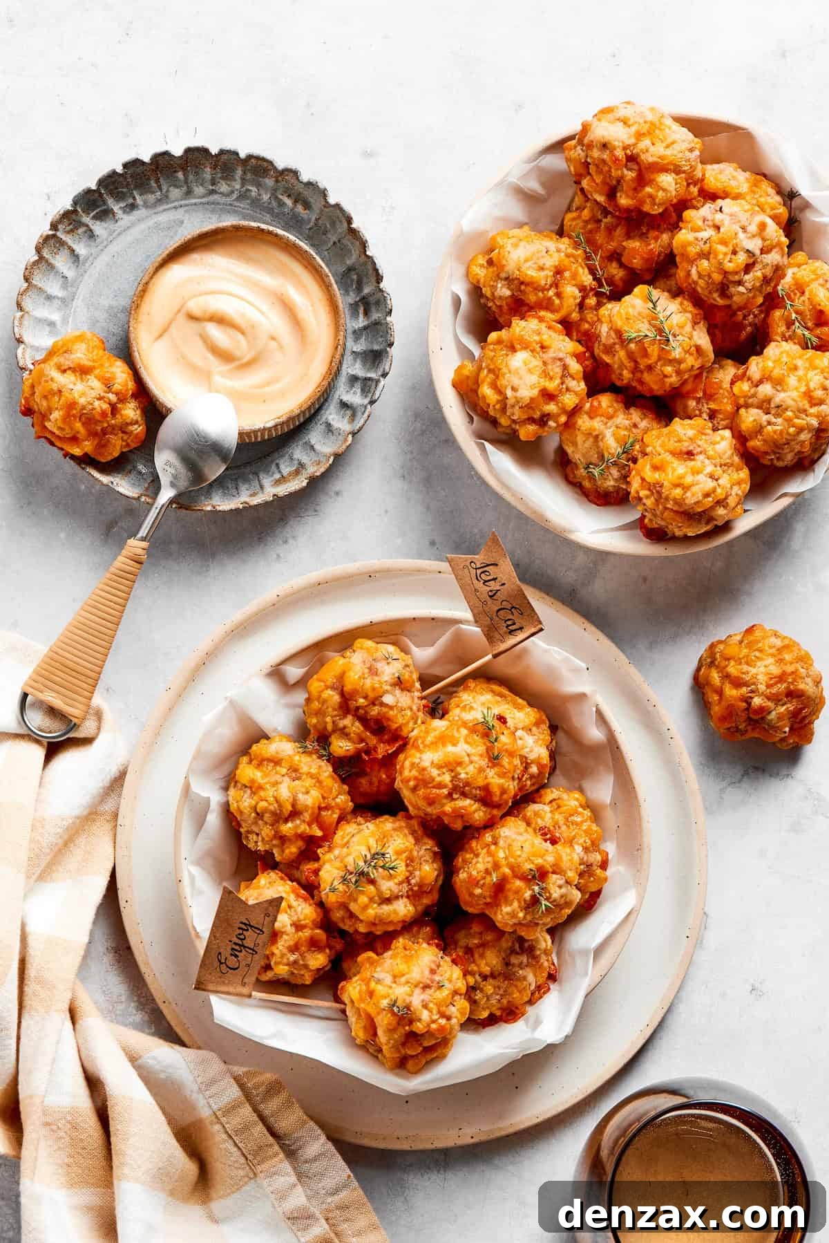 Two bowls filled with freshly baked sausage balls, accompanied by a small bowl of dipping sauce and a serving spoon, inviting indulgence.